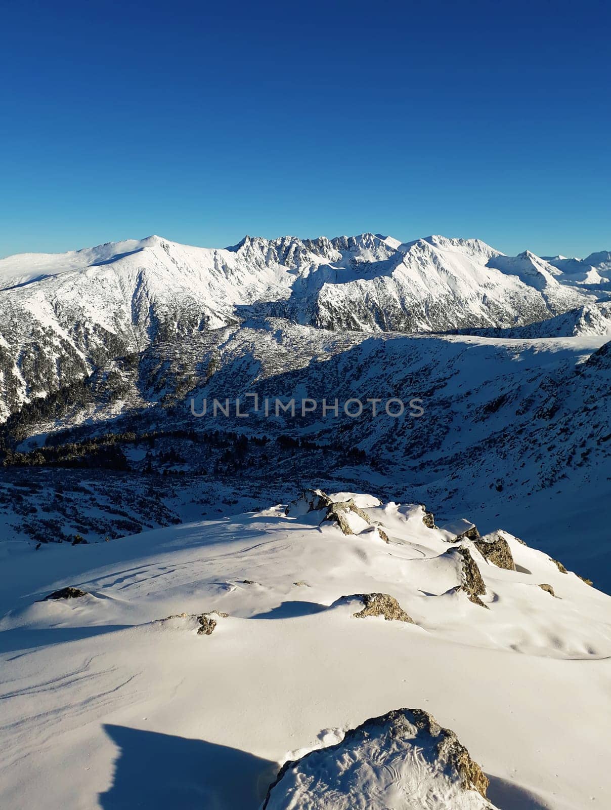 View from the top of Todorka Peak to the Pirin mountains ridge covered by snow in a sunny winter day with blue sky.