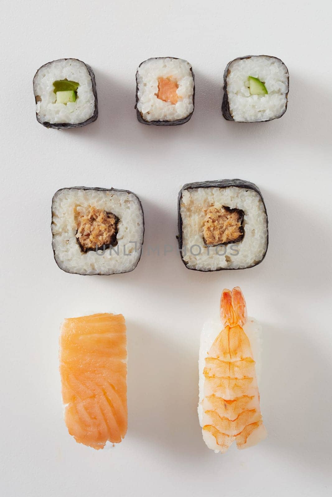 Assorted fresh sushi arranged on white with raw salmon nigiri, prawn or lobster sashimi and maki rolls with nori seaweed