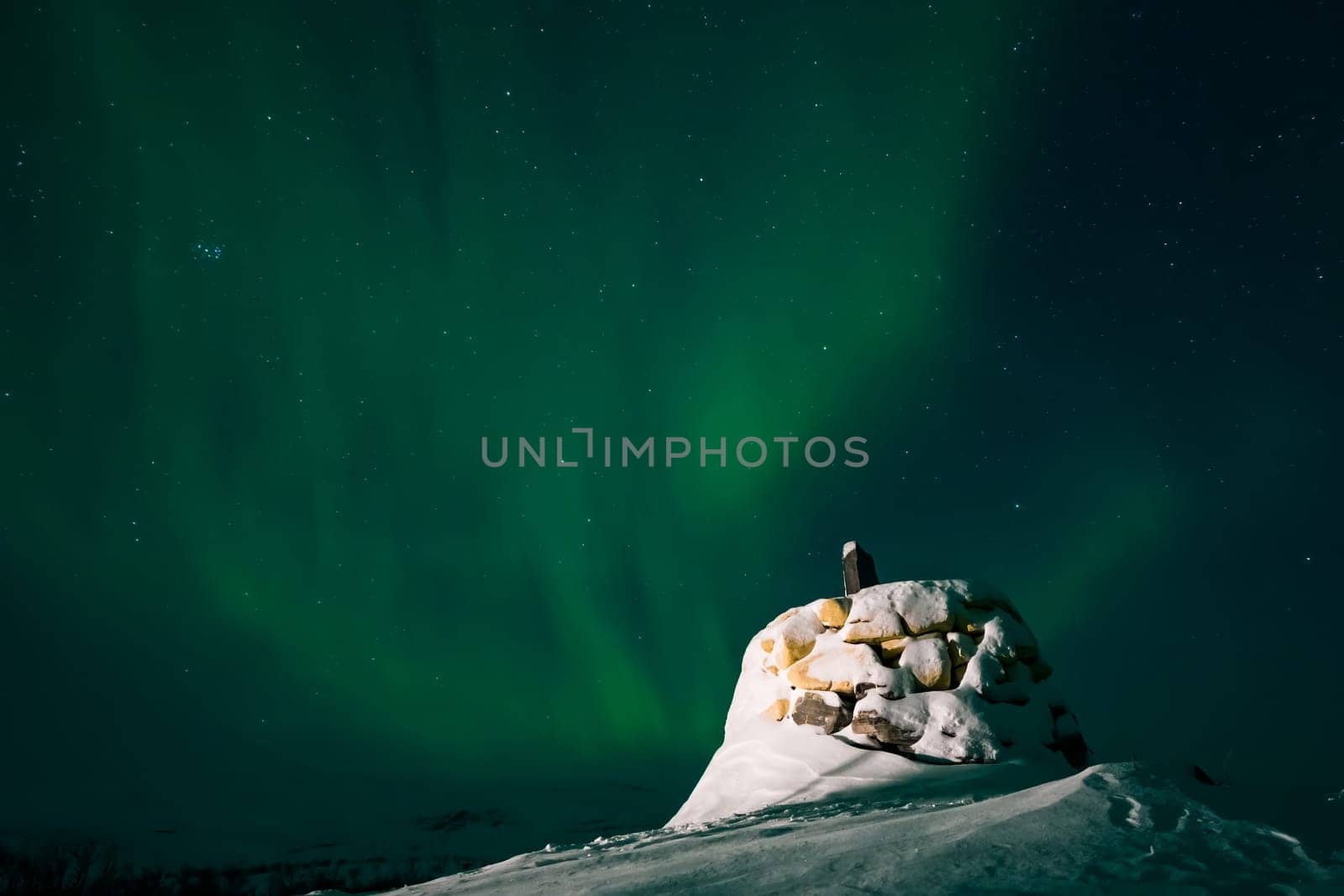 Awesome display of aurora borealis northern lights above the stone marker on the border between Finland and Norway