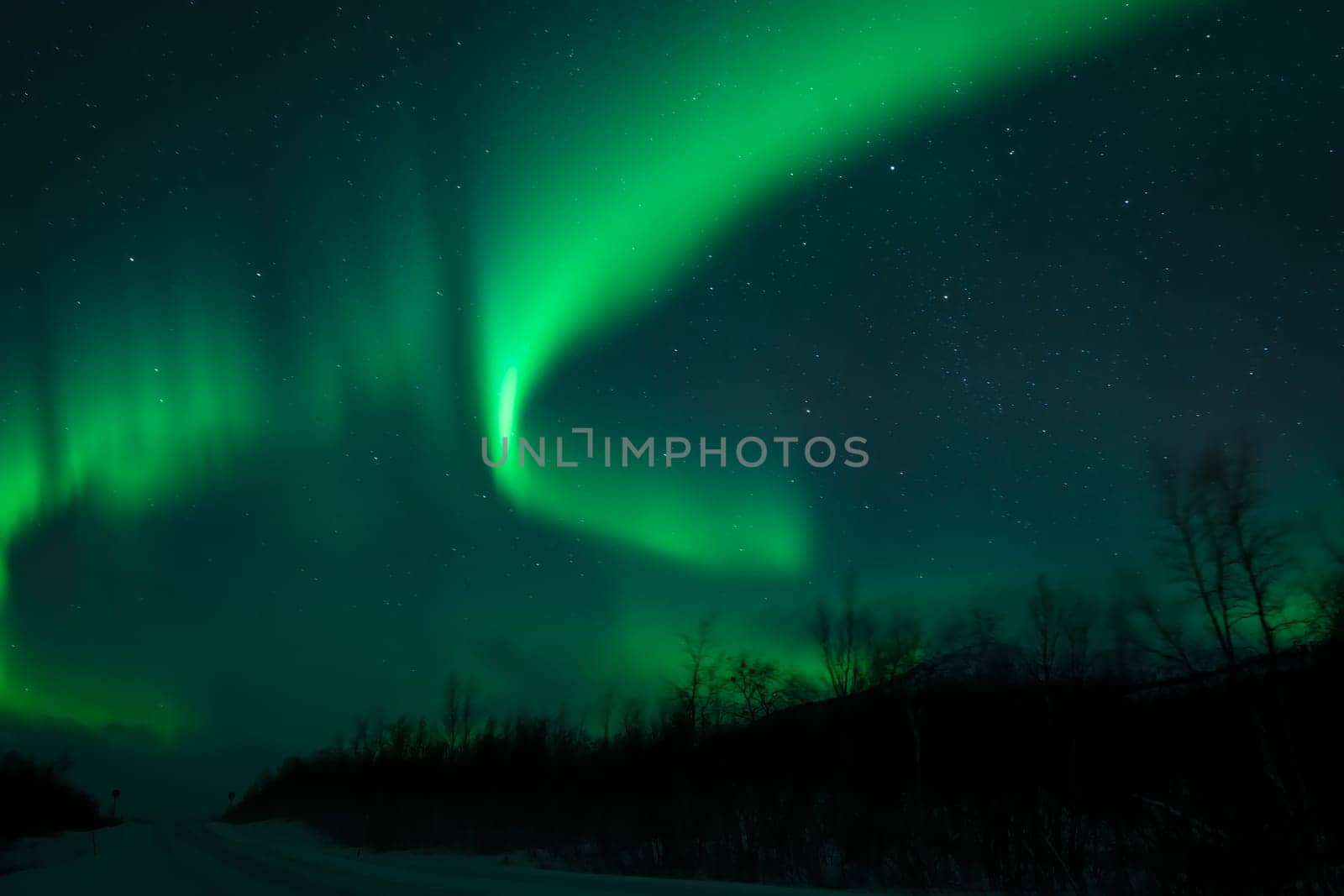 Awesome display of aurora borealis northern lights above empty snow covered road in Norway and Finland