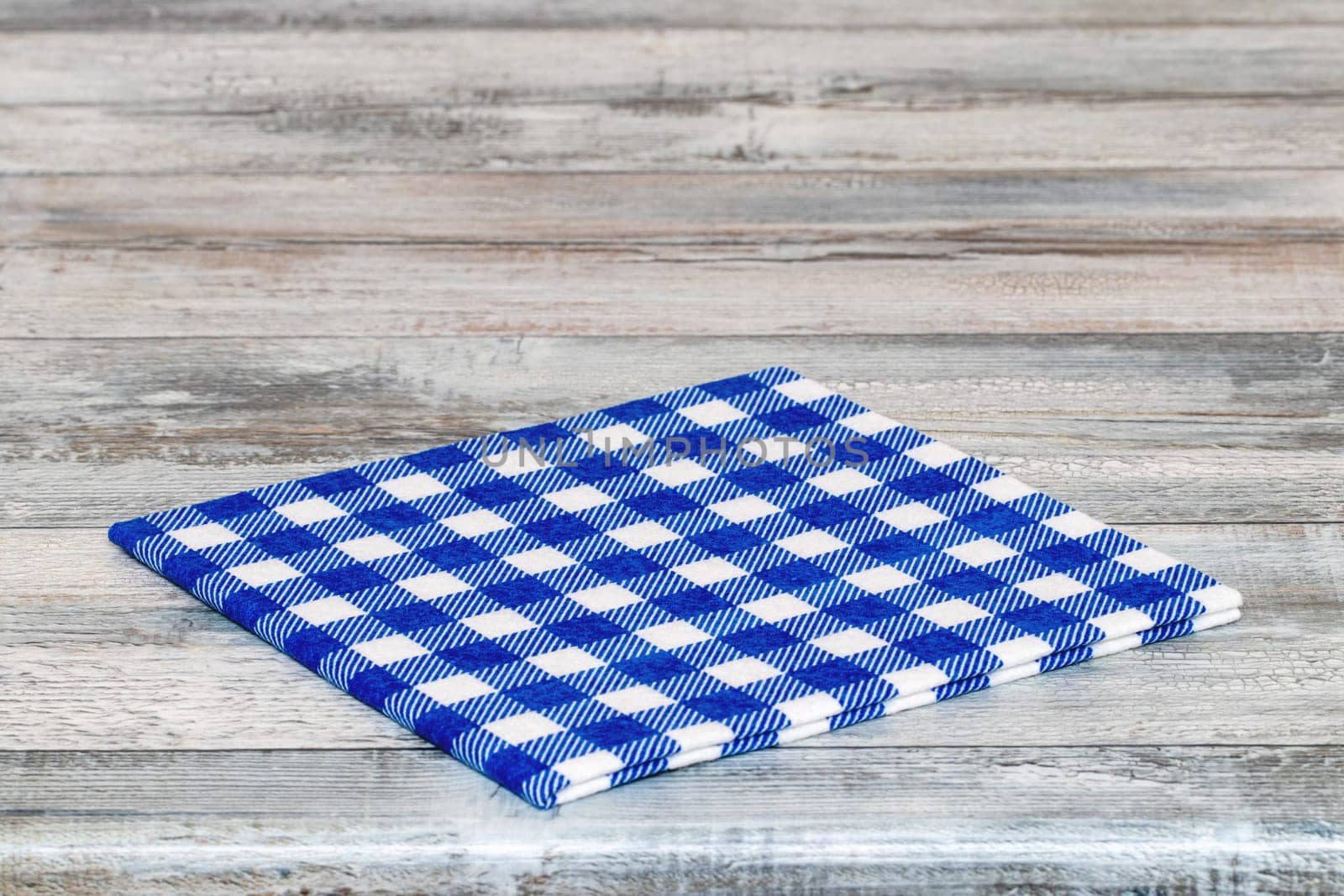 Empty table background. Closeup of a empty blue and white checkered kitchen cloth, textile, tablecloth or napkin on a rustic bright gray table. Template for food and product display montage. Macro.