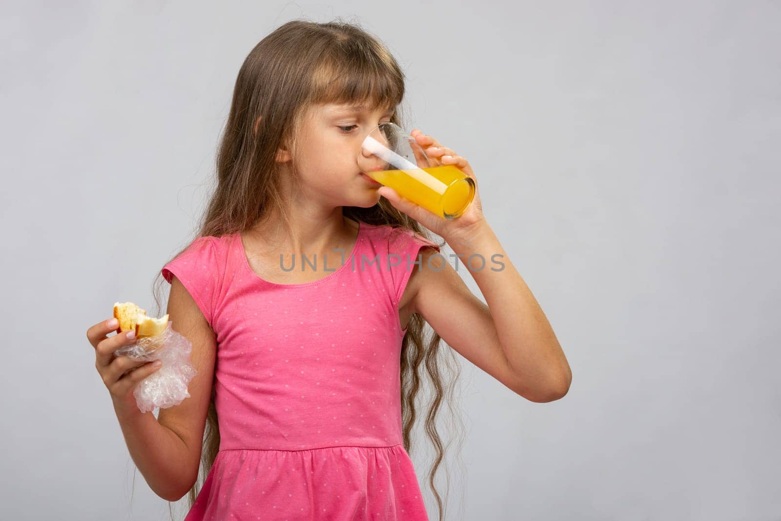 A girl drinks orange juice and eats a bun