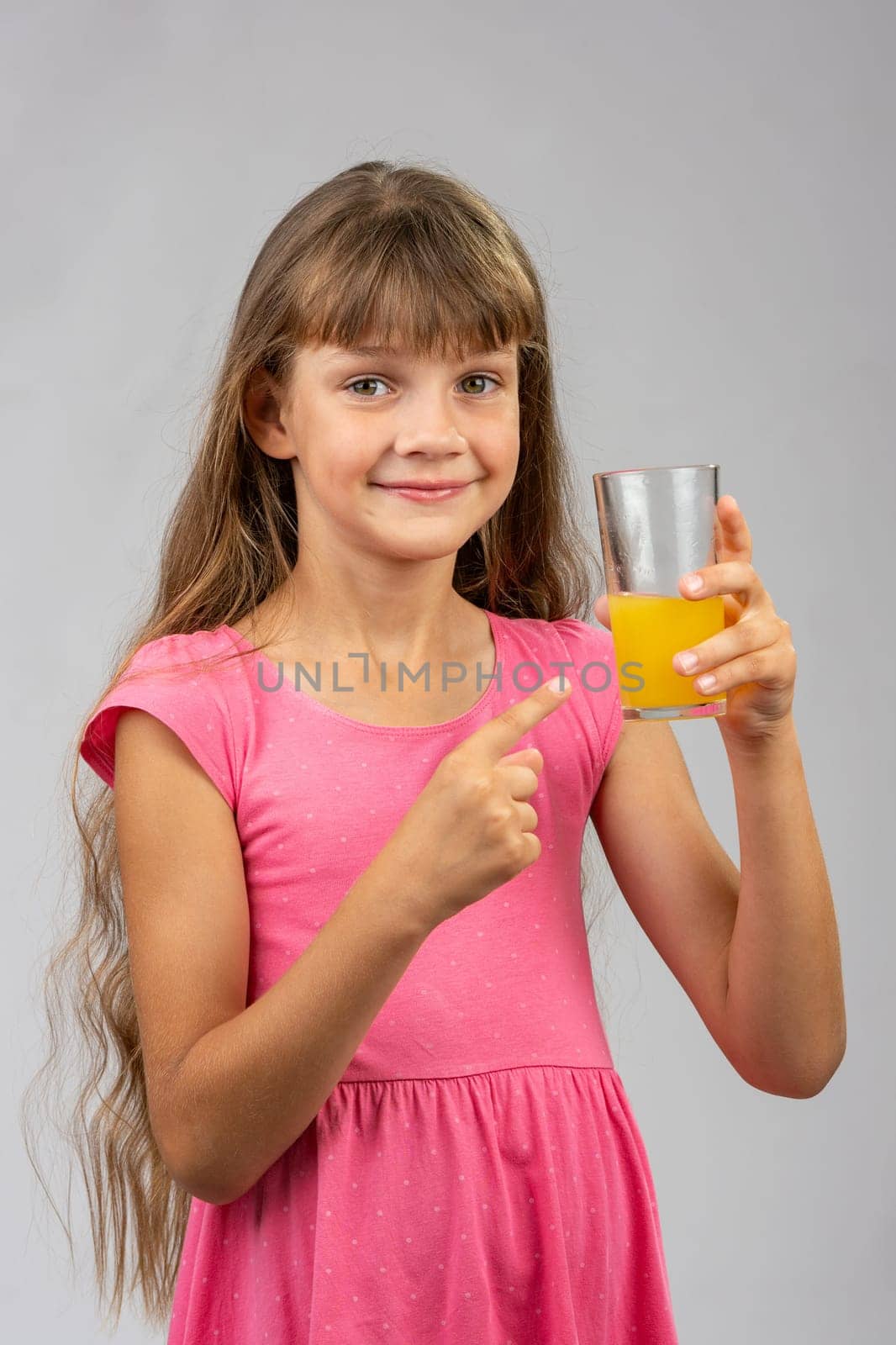 A girl holds a glass of orange juice in her hand and points her finger at it