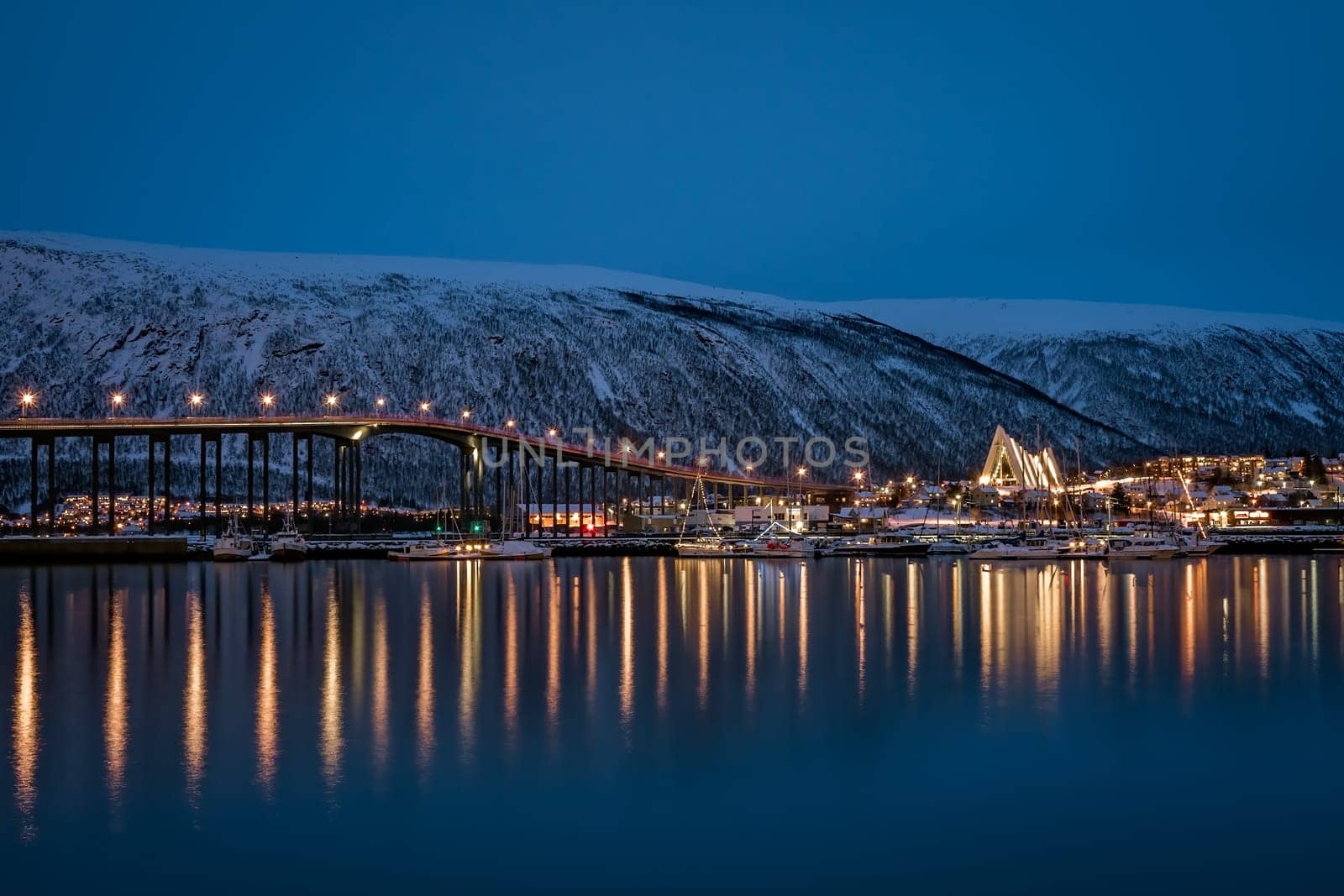 Tromso, Norway -  December 2018 : Port and harbour with famous Tromso Bridge across Tromsoysundet strait in the background, photographed at night