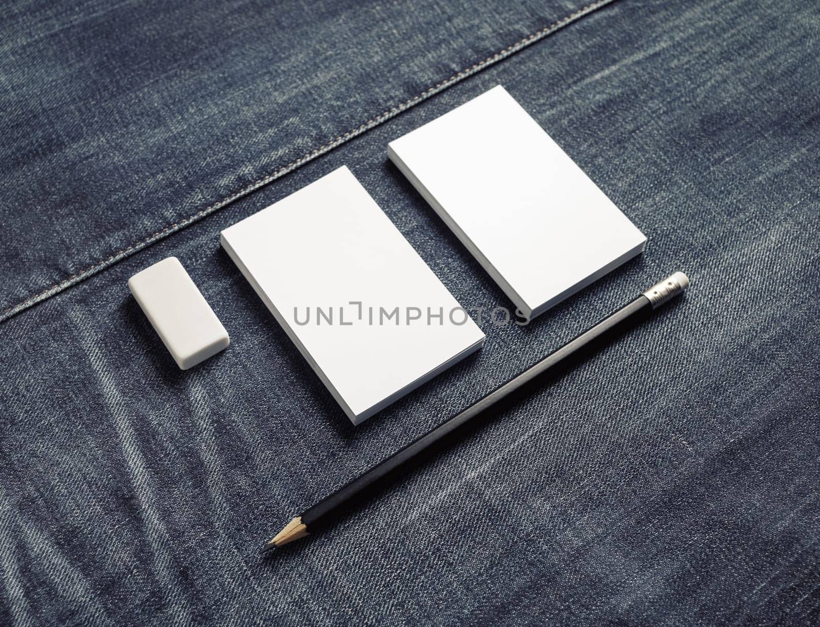 Photo of blank white business cards stacks, pencil and eraser on denim background. Stationery mock up.