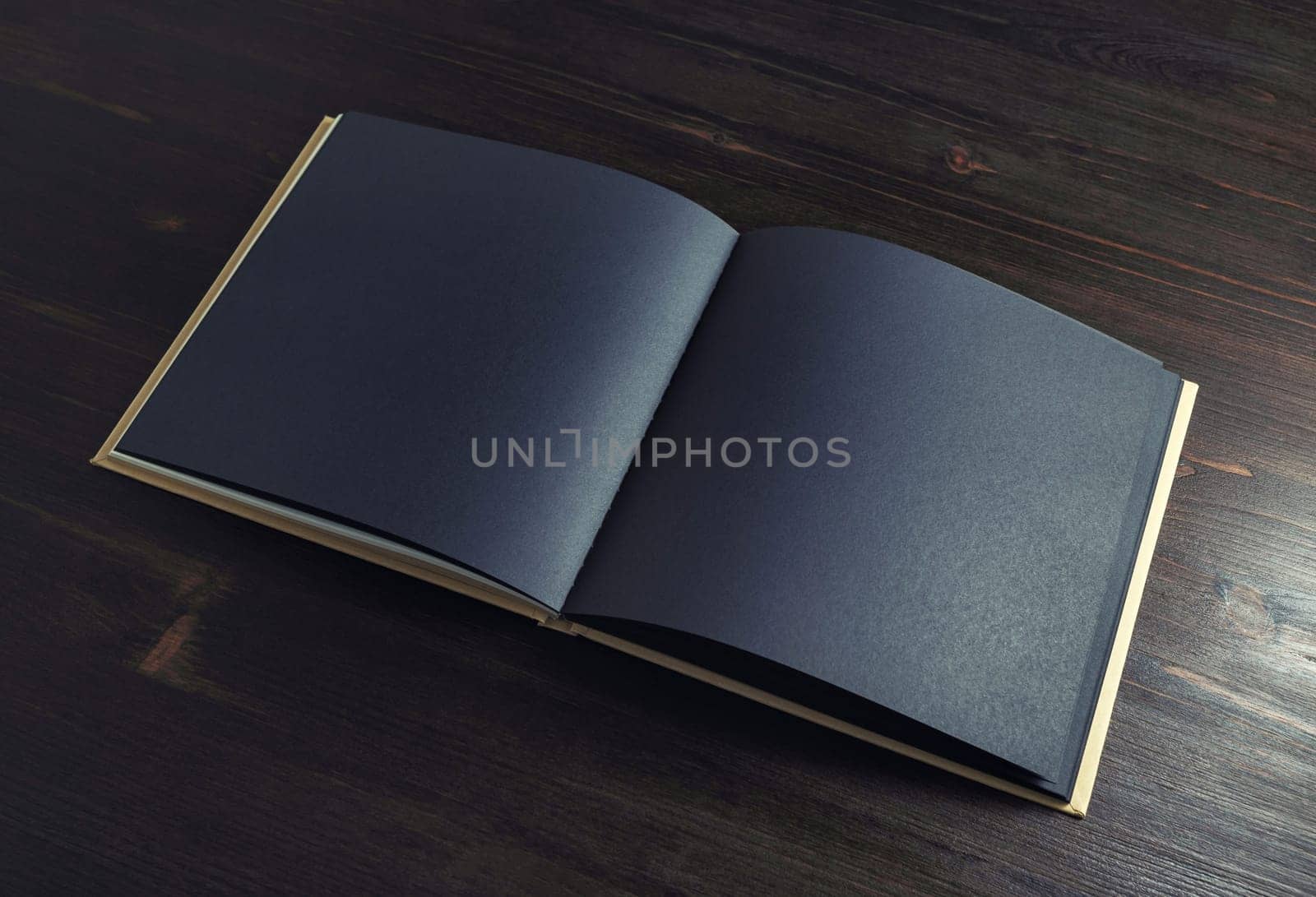 Booklet with blank black pages on dark wood table background.