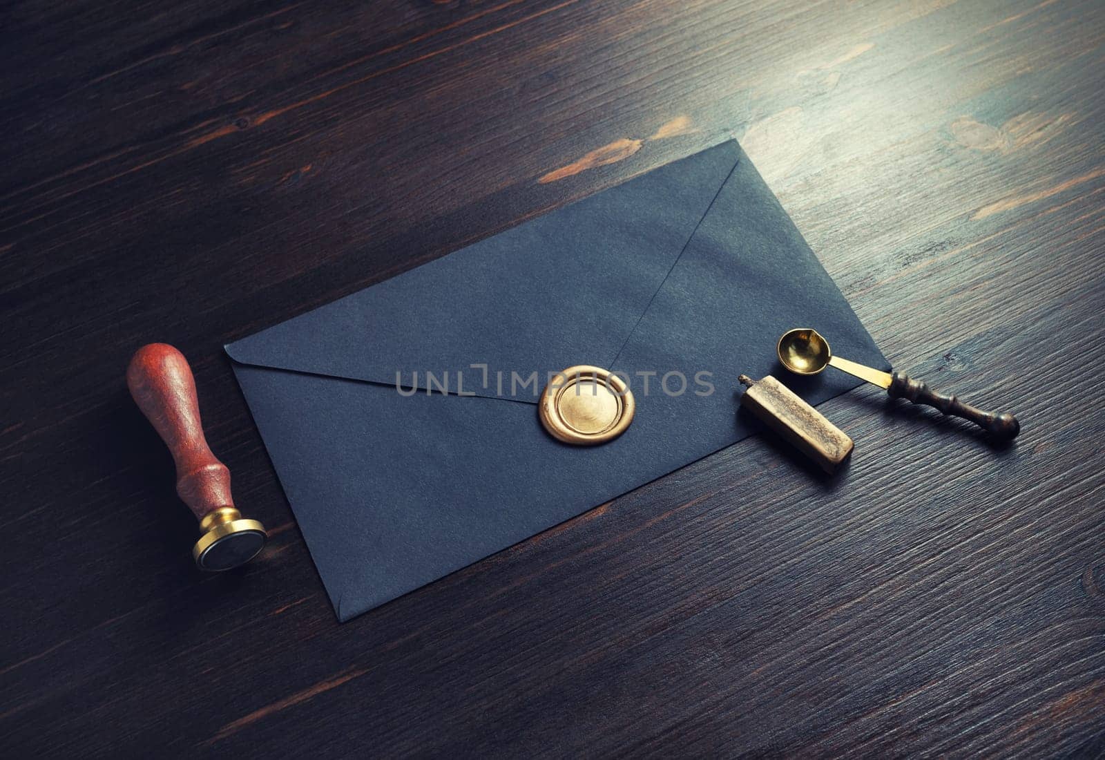 Photo of vintage black envelope with wax seal, stamp and spoon on dark wood table background.