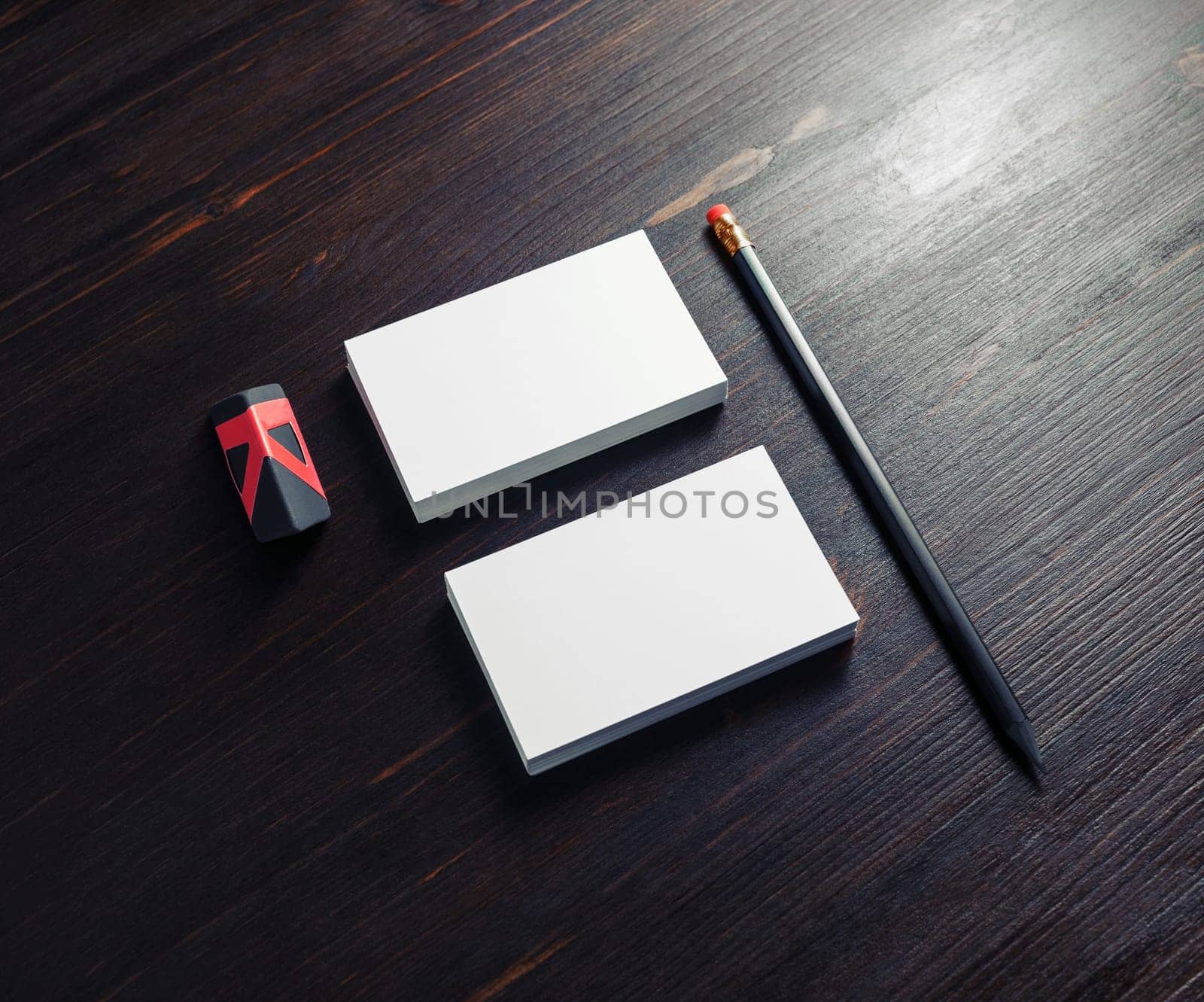 Blank office stationery. White business cards, pencil and black eraser on dark wooden background.