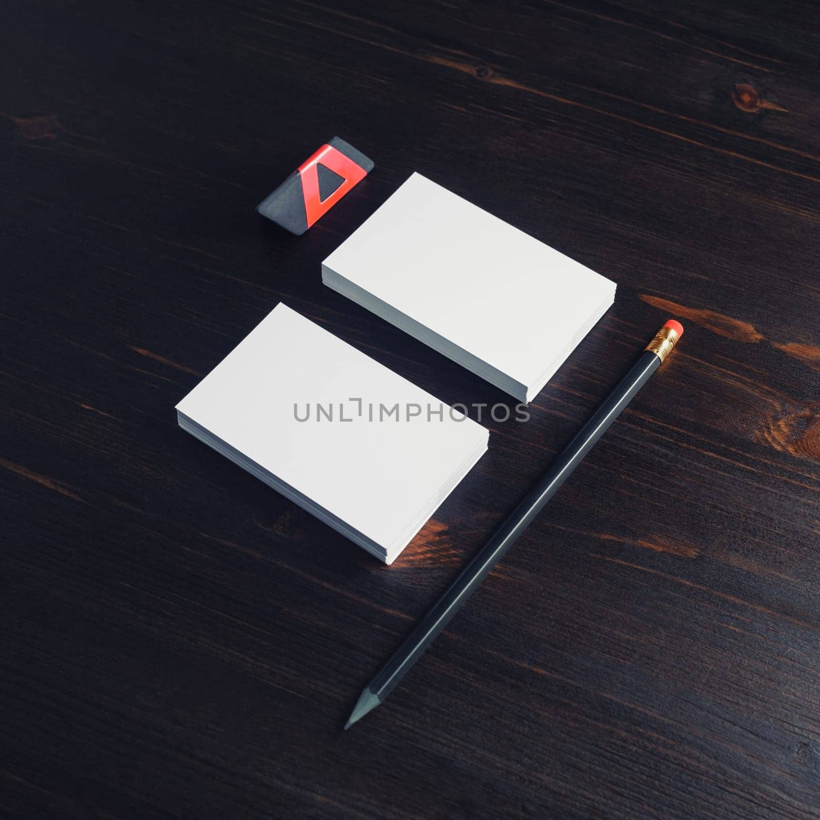 White business cards, pencil and black eraser on dark wood table background.