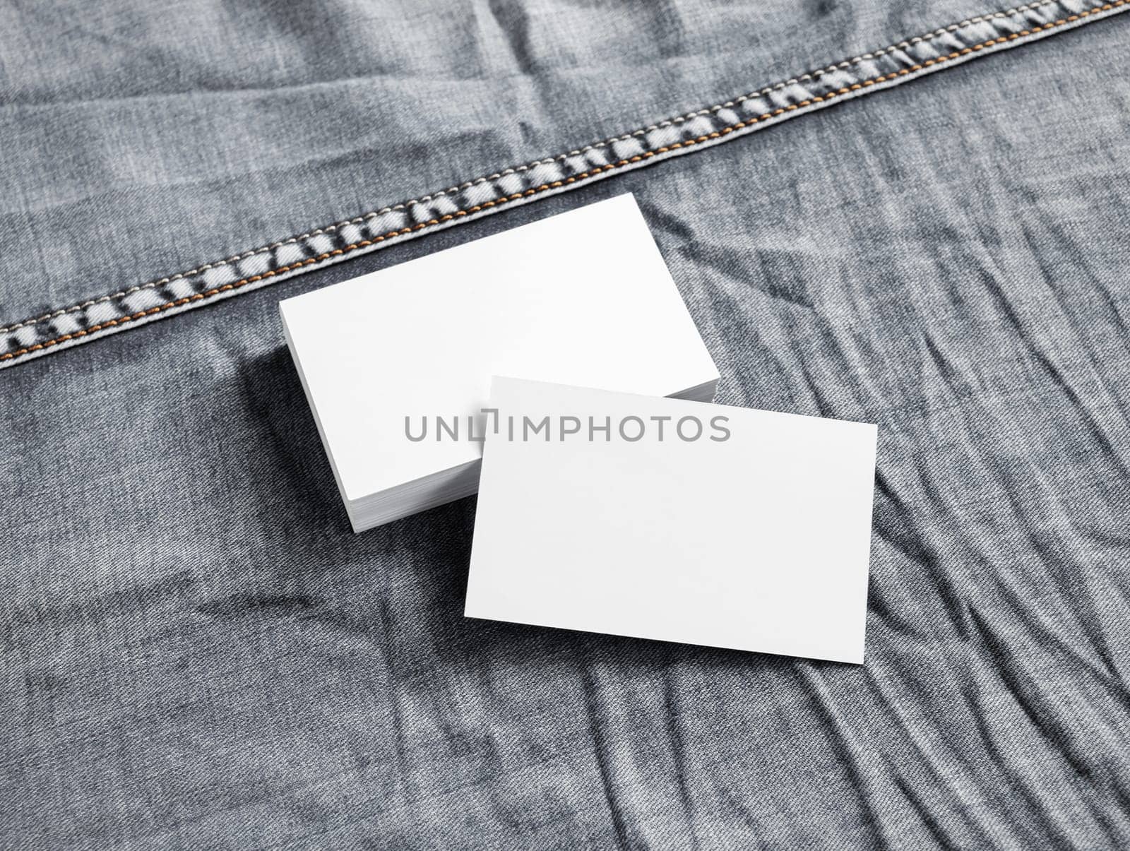 Blank white paper business cards on gray denim background.