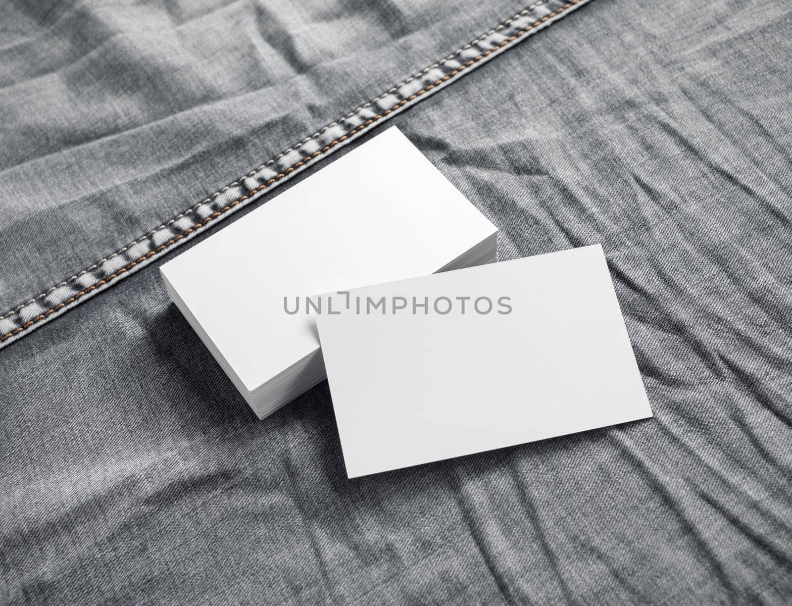 Blank white business cards on gray denim background.