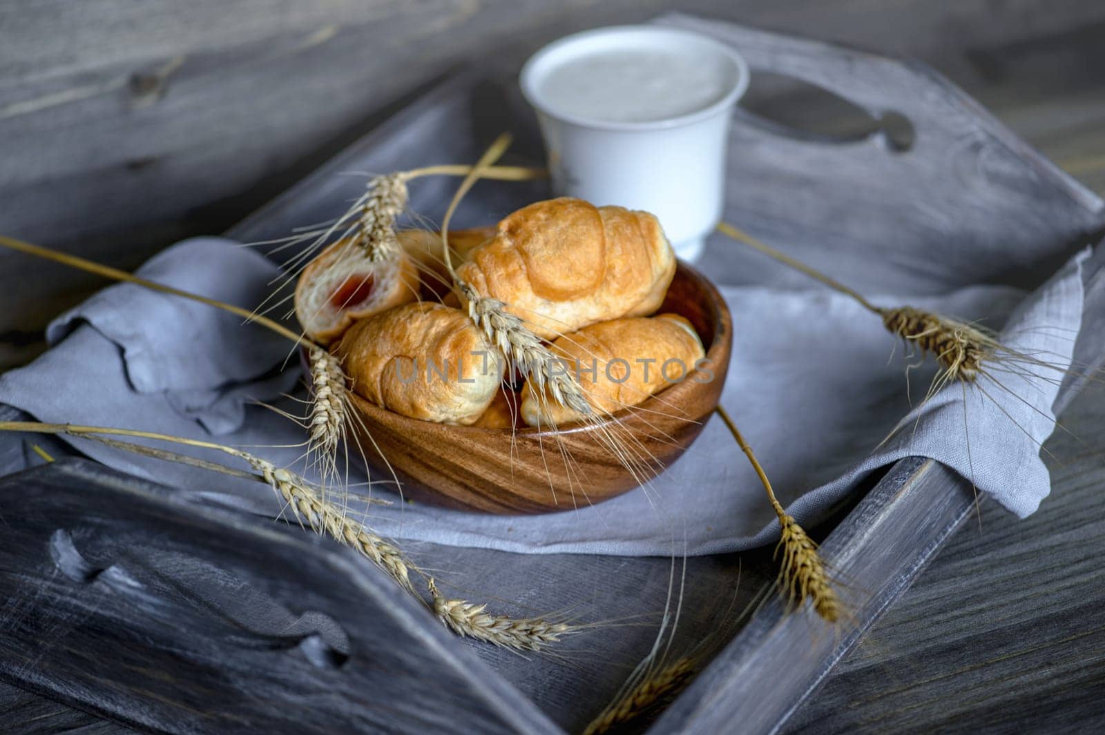 Croissants, a cup with kefir and ears of grain on a wooden tray. The concept of a wholesome breakfast