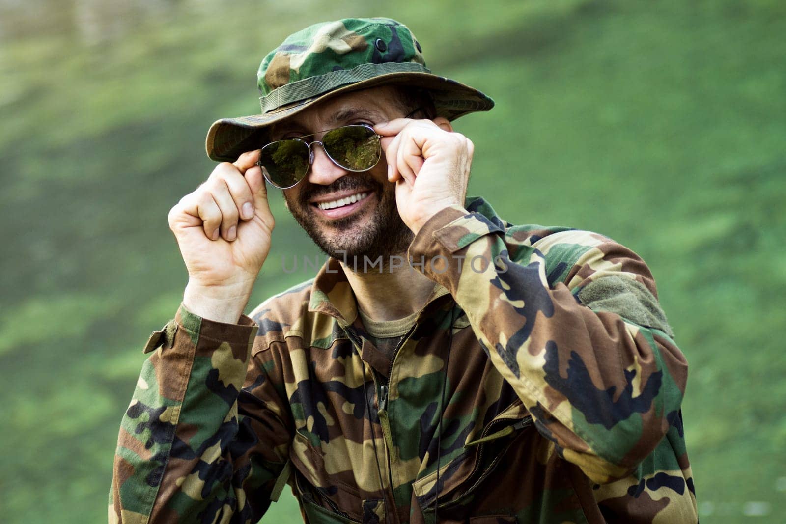 Portrait of smiling park ranger in military uniform and sunglasses on green background.