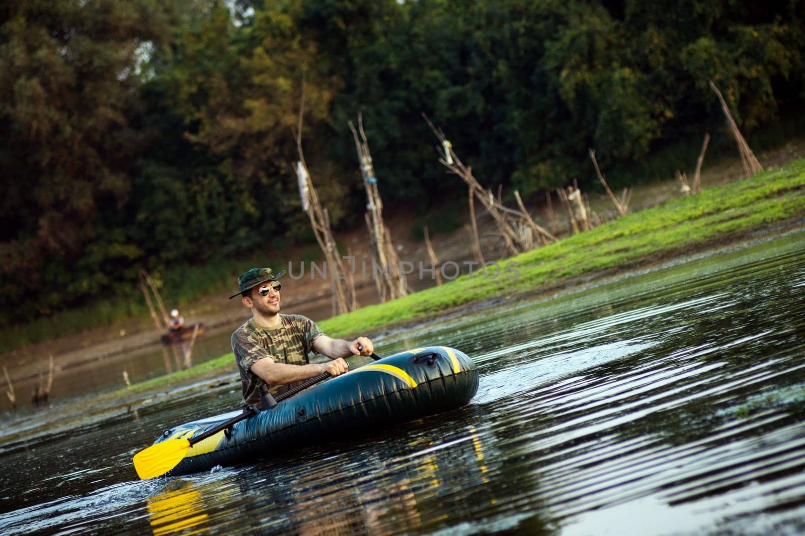 The oarsman is rowing in inflatable boat on shallow lake in nature.