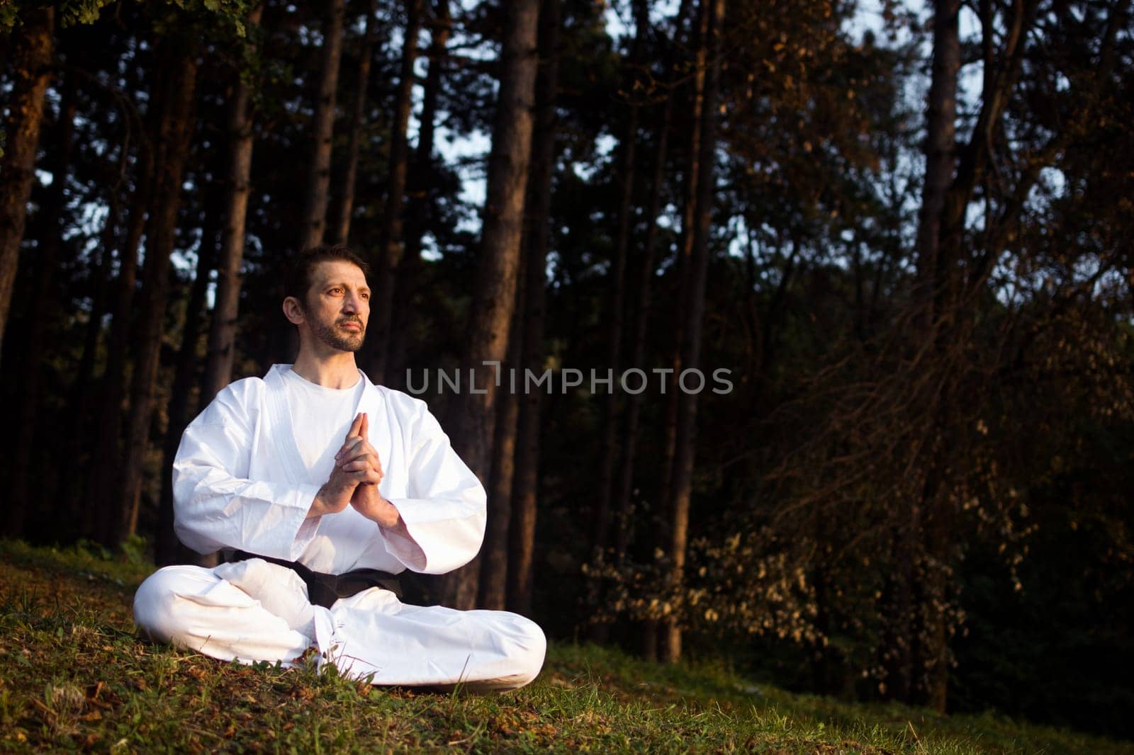 Man in white kimono is practicing meditation in nature in forest.
