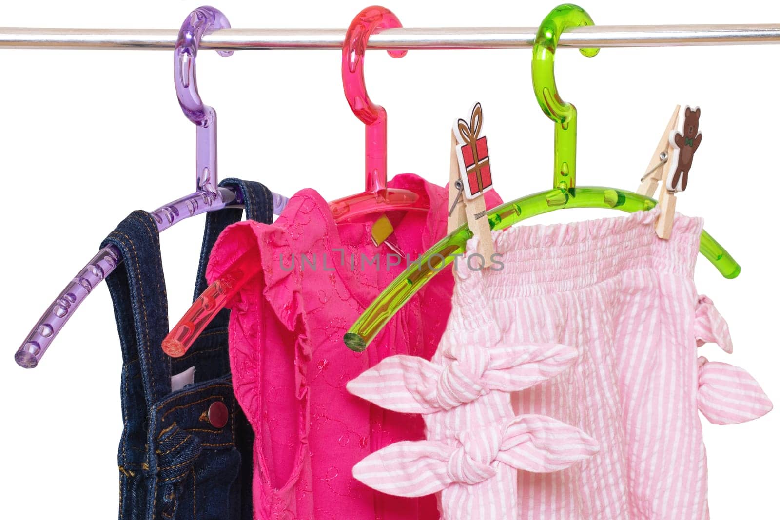 Girls clothes on rack. Close-up of colorful stylish summer dresses and a short pants for the little girl on a rack isolated on a white background. Clothes for kids on hanger. Macro.