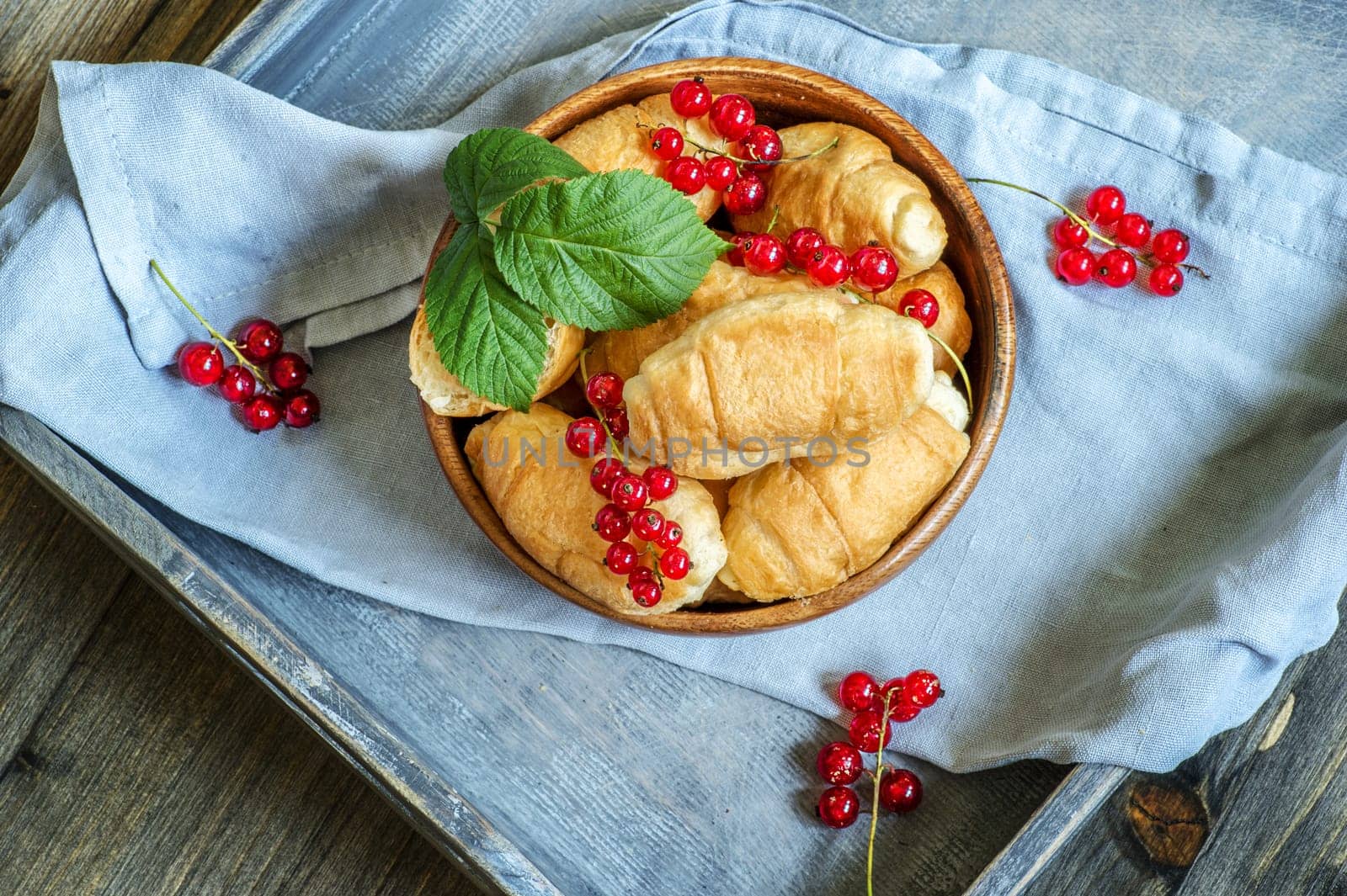 Croissants with currant berries on a wooden tray. The concept of a wholesome breakfast