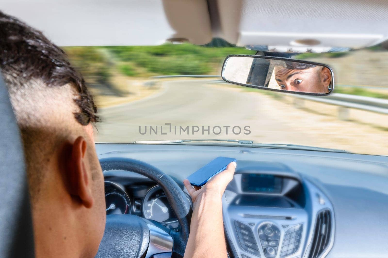 Young driver, using smartphone, on the road in the car. Distraction and danger on the road.