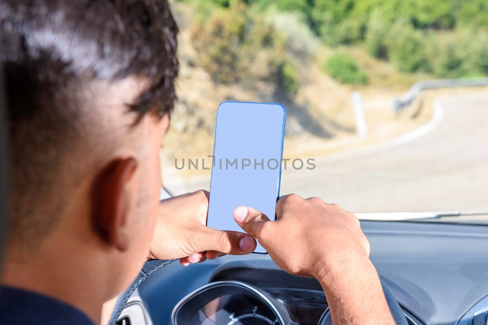 Young driver, using smartphone, on the road in the car. Distraction and danger on the road.
