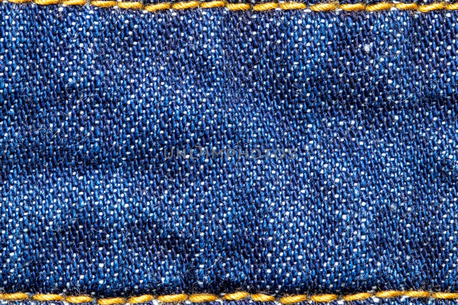 Denim background texture. Close-up of blue jeans fabric frame with simple yellow seam at the top and bottom. Large copy space for design. Beautiful backdrop. Macro.