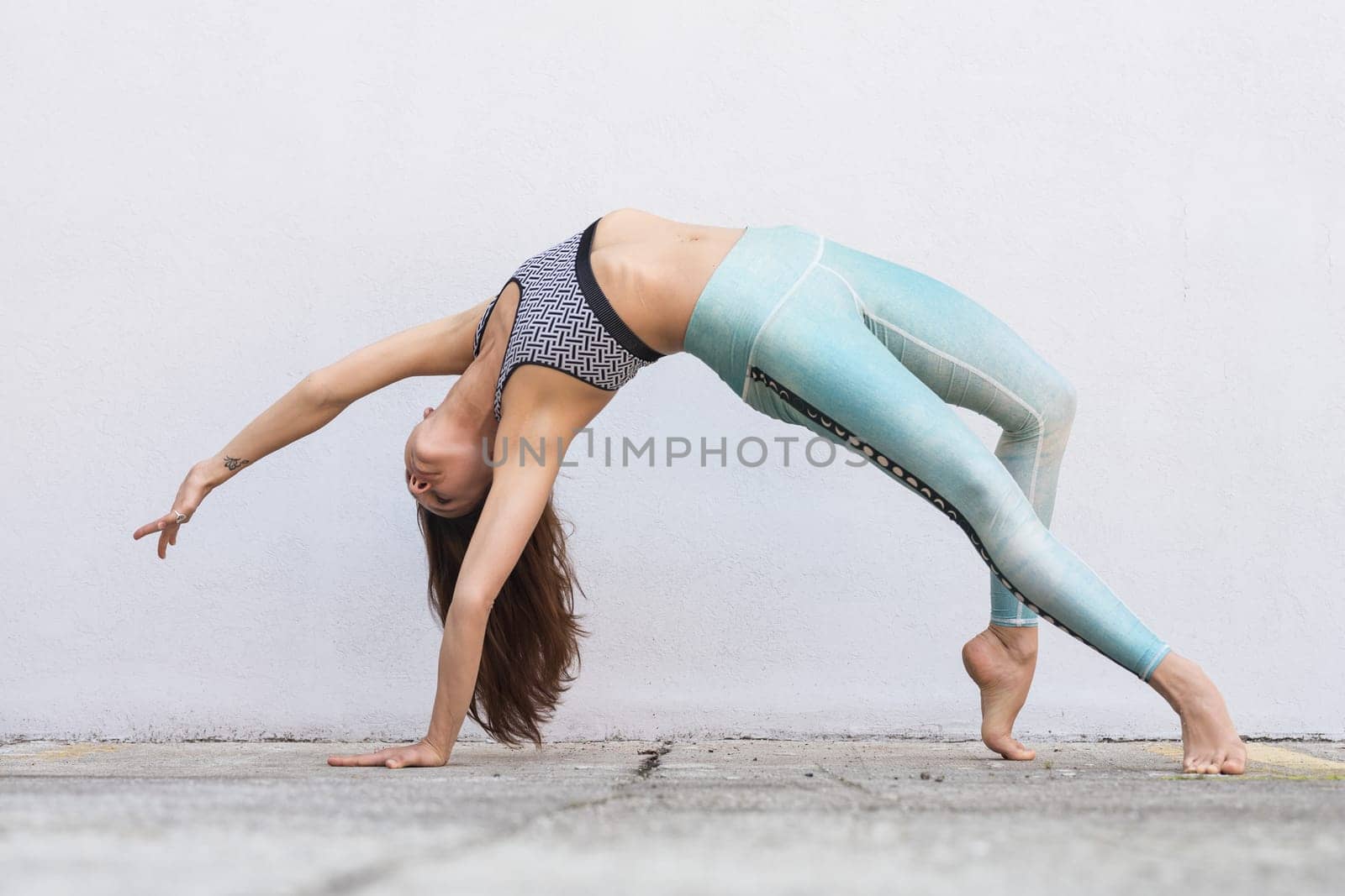 Fit sporty active girl in fashion sportswear doing yoga fitness exercise in front of gray wall, outdoor sports, urban style.