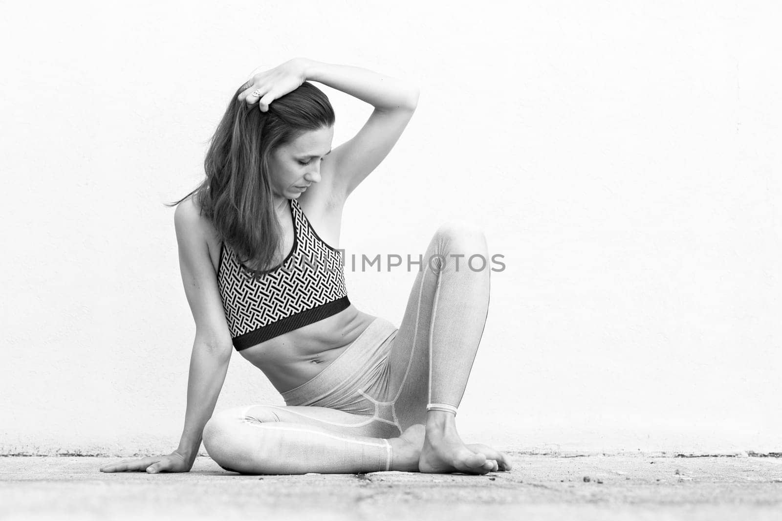 Fit sporty active girl in fashion sportswear sitting on the floor in front of gray wall. Outdoor sports, active urban lifestyle concept. Black and white image.