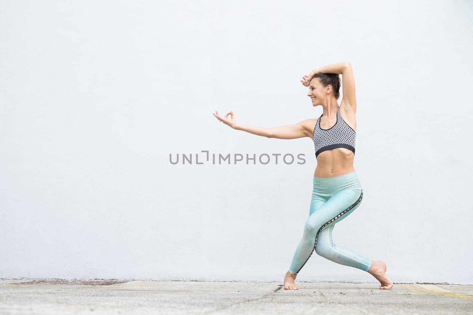 Fit sporty active girl in fashion sportswear doing yoga fitness exercise in front of gray wall, outdoor sports, urban style.