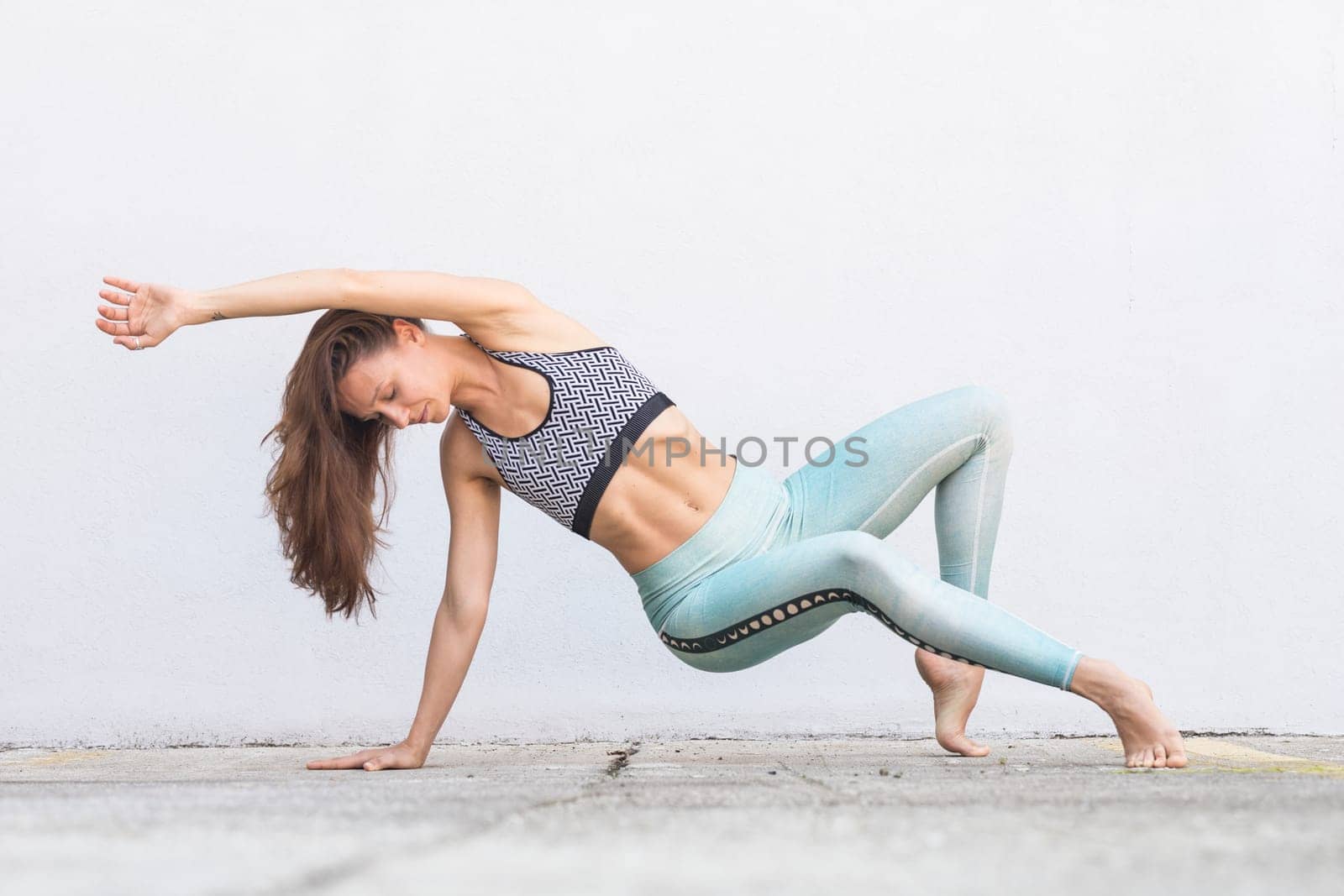 Fit sporty active girl in fashion sportswear doing yoga fitness exercise in front of gray wall, outdoor sports, urban style.