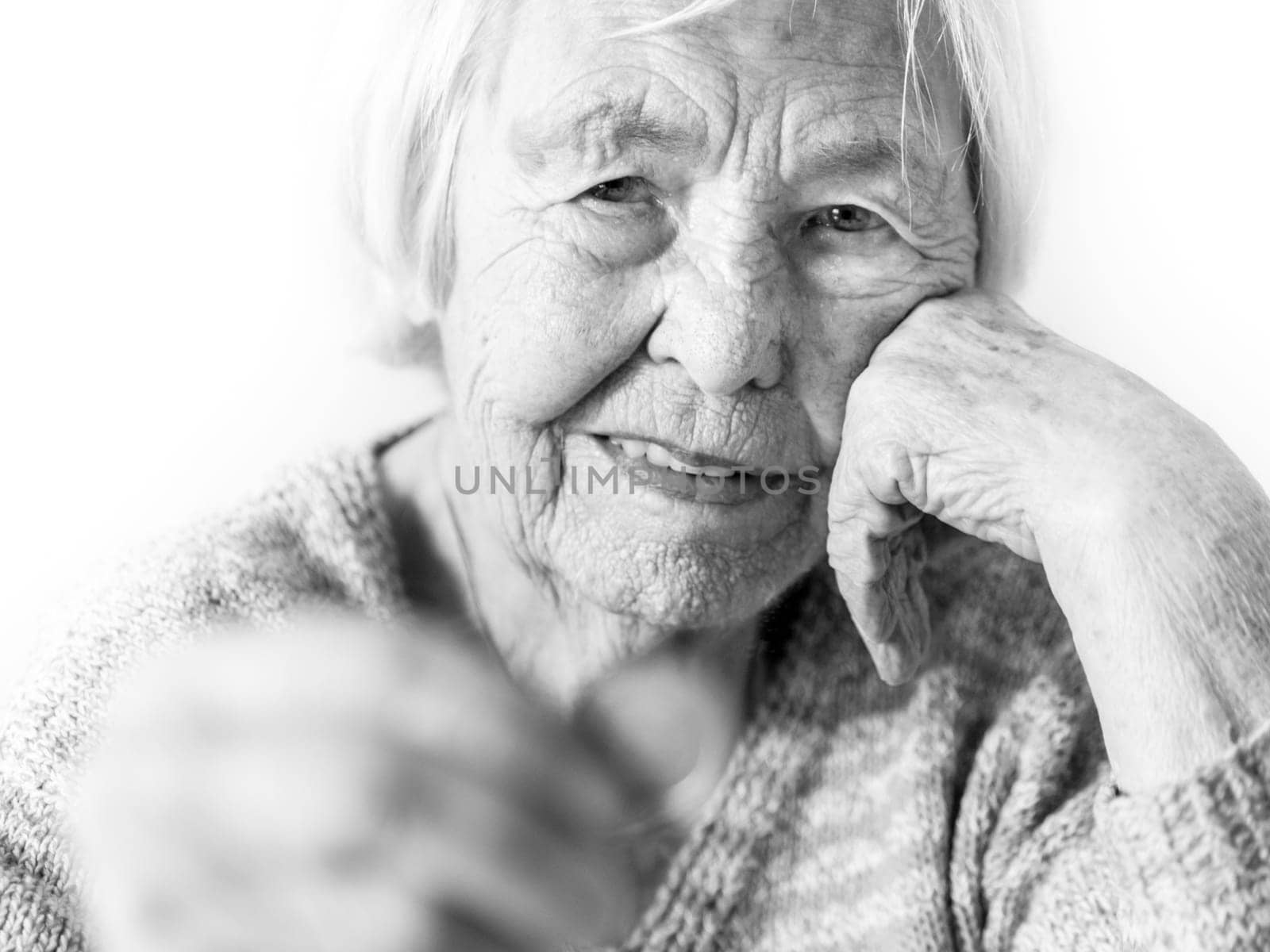 Cheerful elderly 96 years old woman sitting at table at home happy with a coin in her hand. Saving for retirement and financial planing concept. Black and white image.