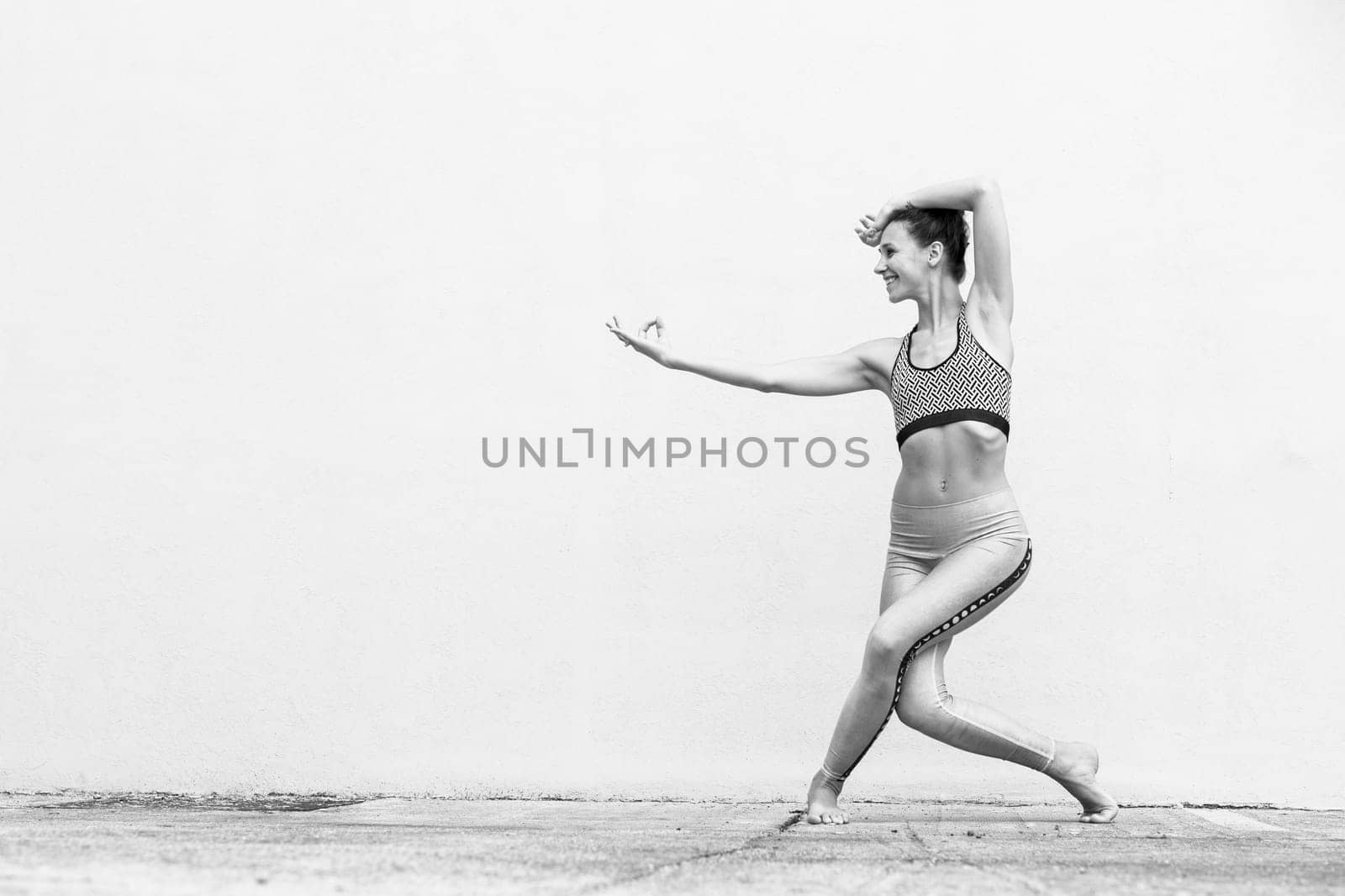 Fit sporty active girl in fashion sportswear doing yoga fitness exercise in front of gray wall, outdoor sports, urban style. Black and white image.
