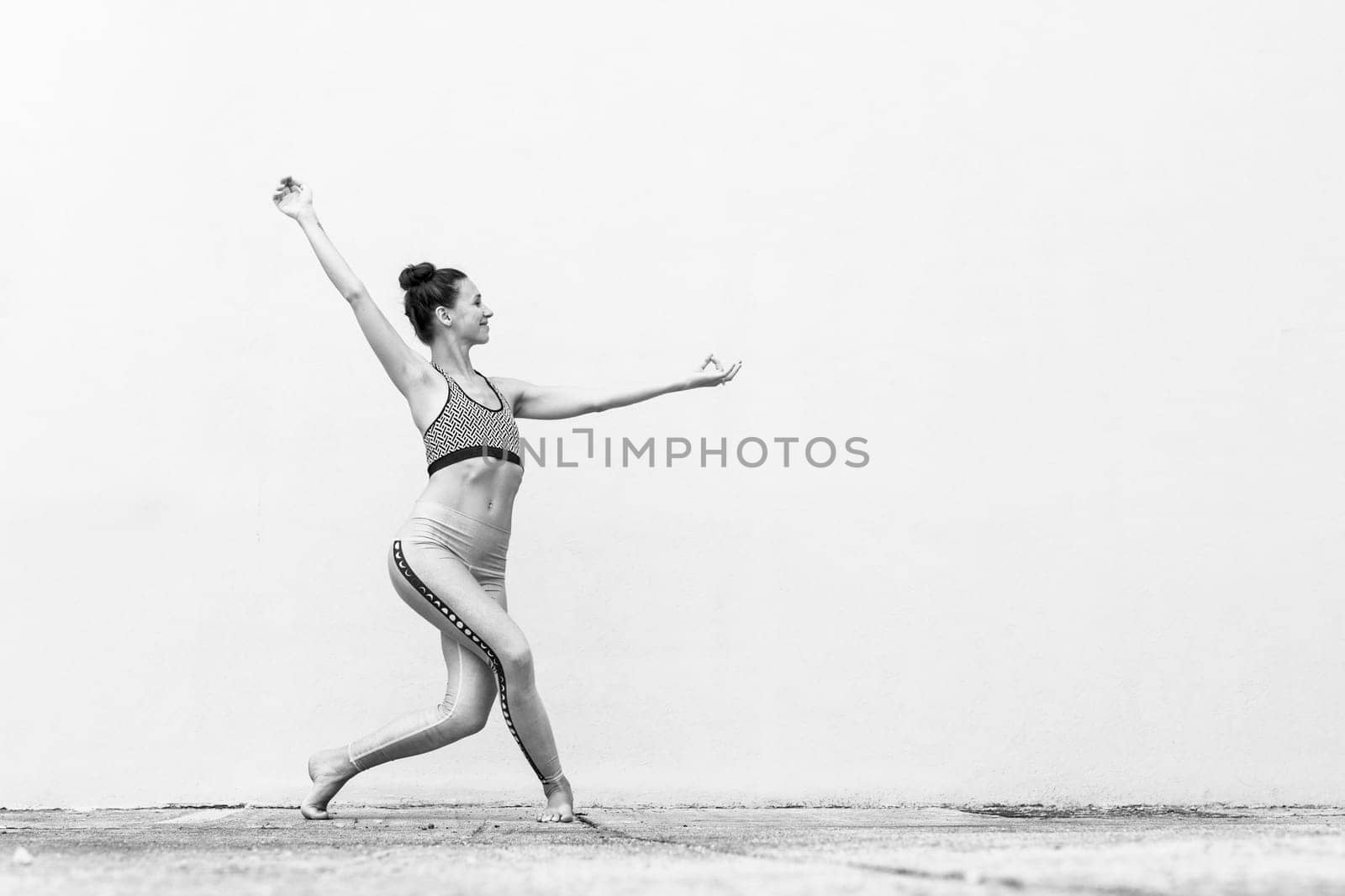 Fit sporty active girl in fashion sportswear doing yoga fitness exercise in front of gray wall, outdoor sports, urban style. Black and white image.