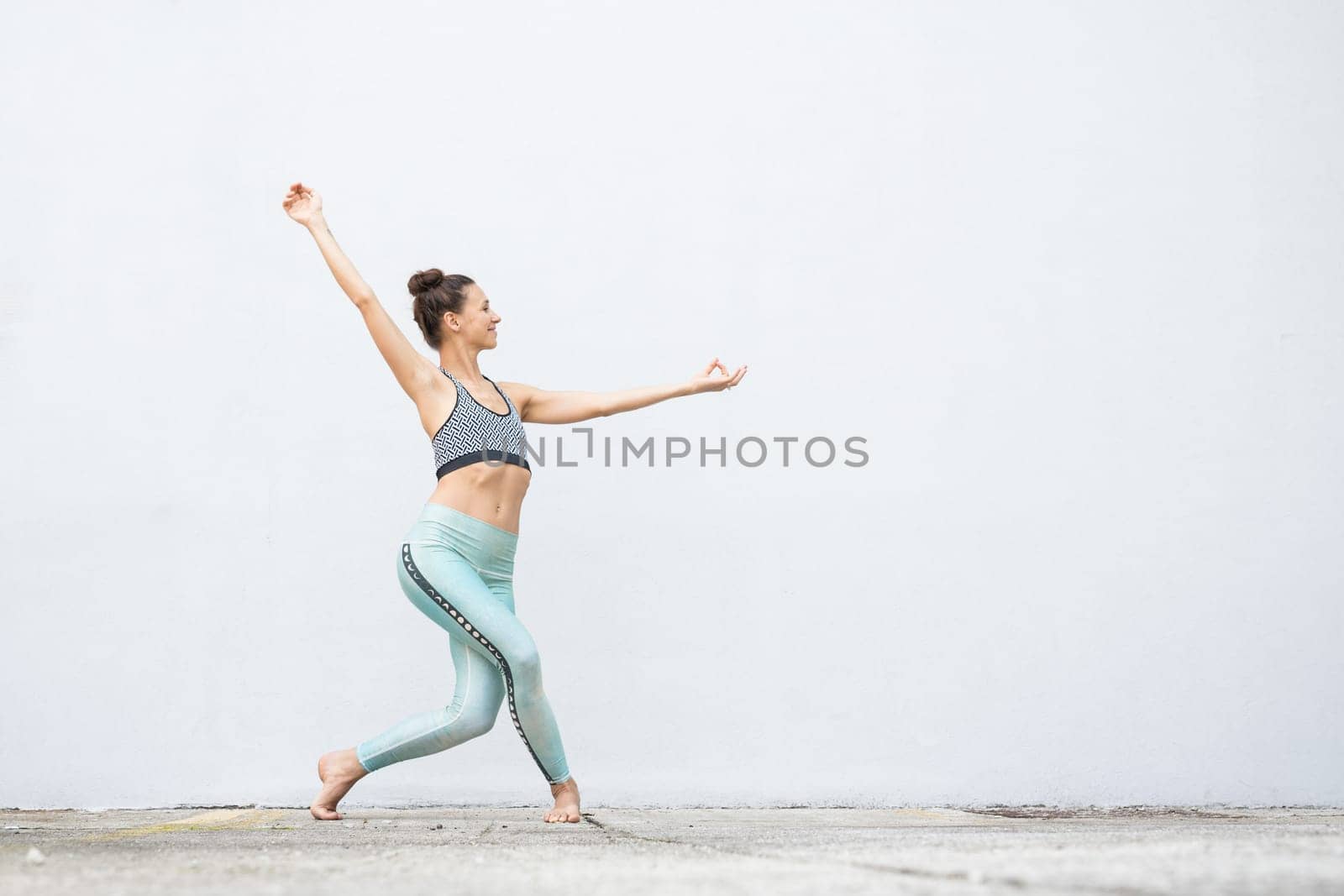 Fit sporty active girl in fashion sportswear doing yoga fitness exercise in front of gray wall, outdoor sports, urban style.