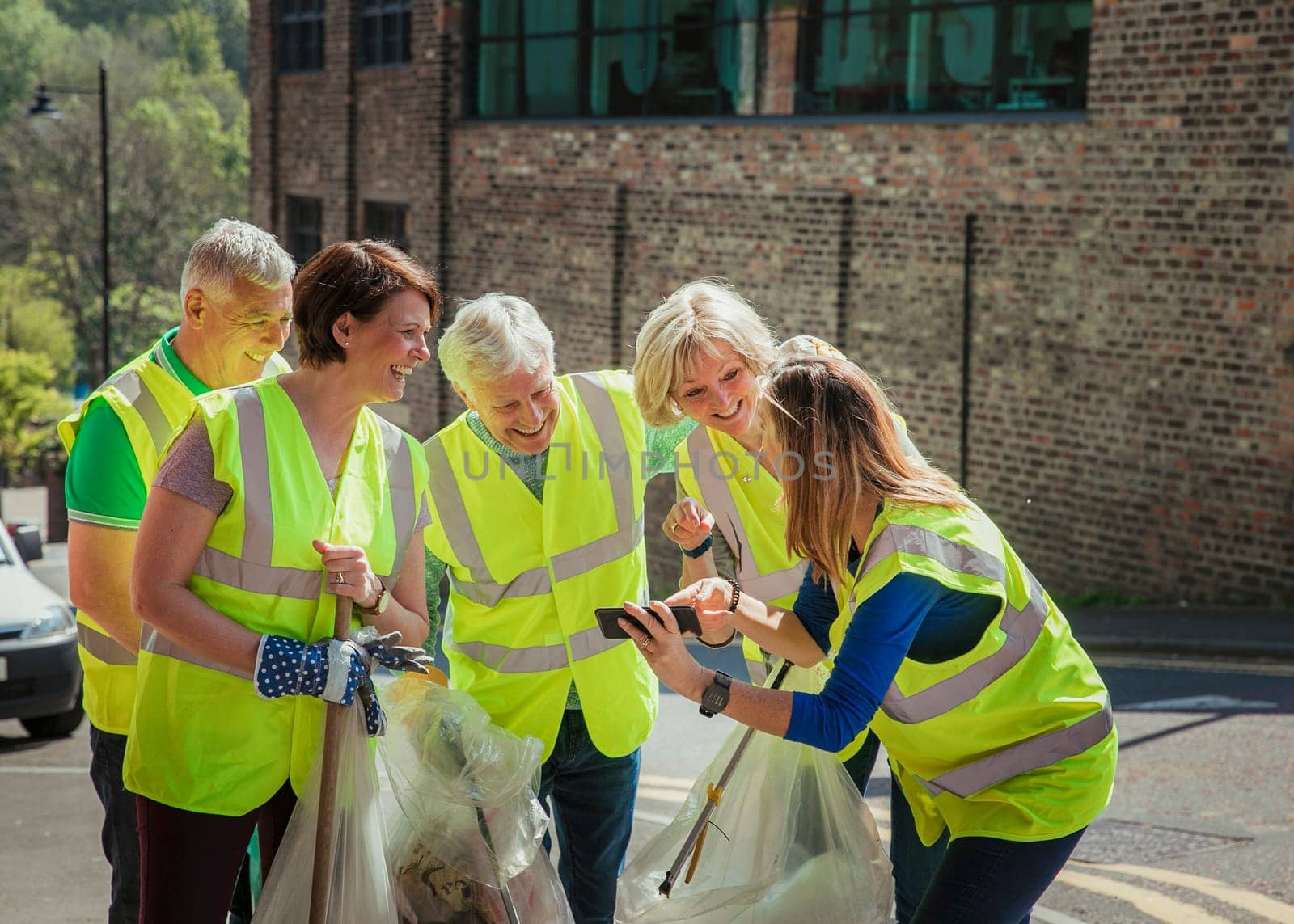 A group of five people taking a selfie. They are wearing high visibility jackets and are participating in a city clean-up.