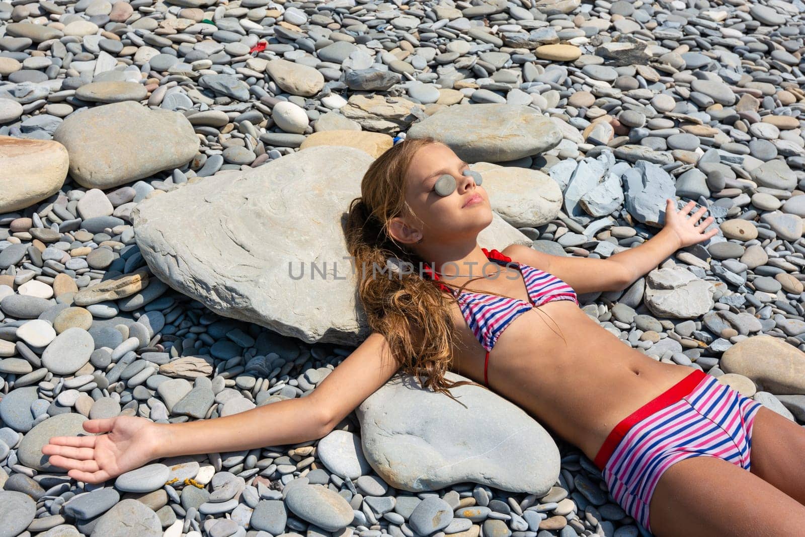 A girl lies on the stones of a rocky beach and sunbathes