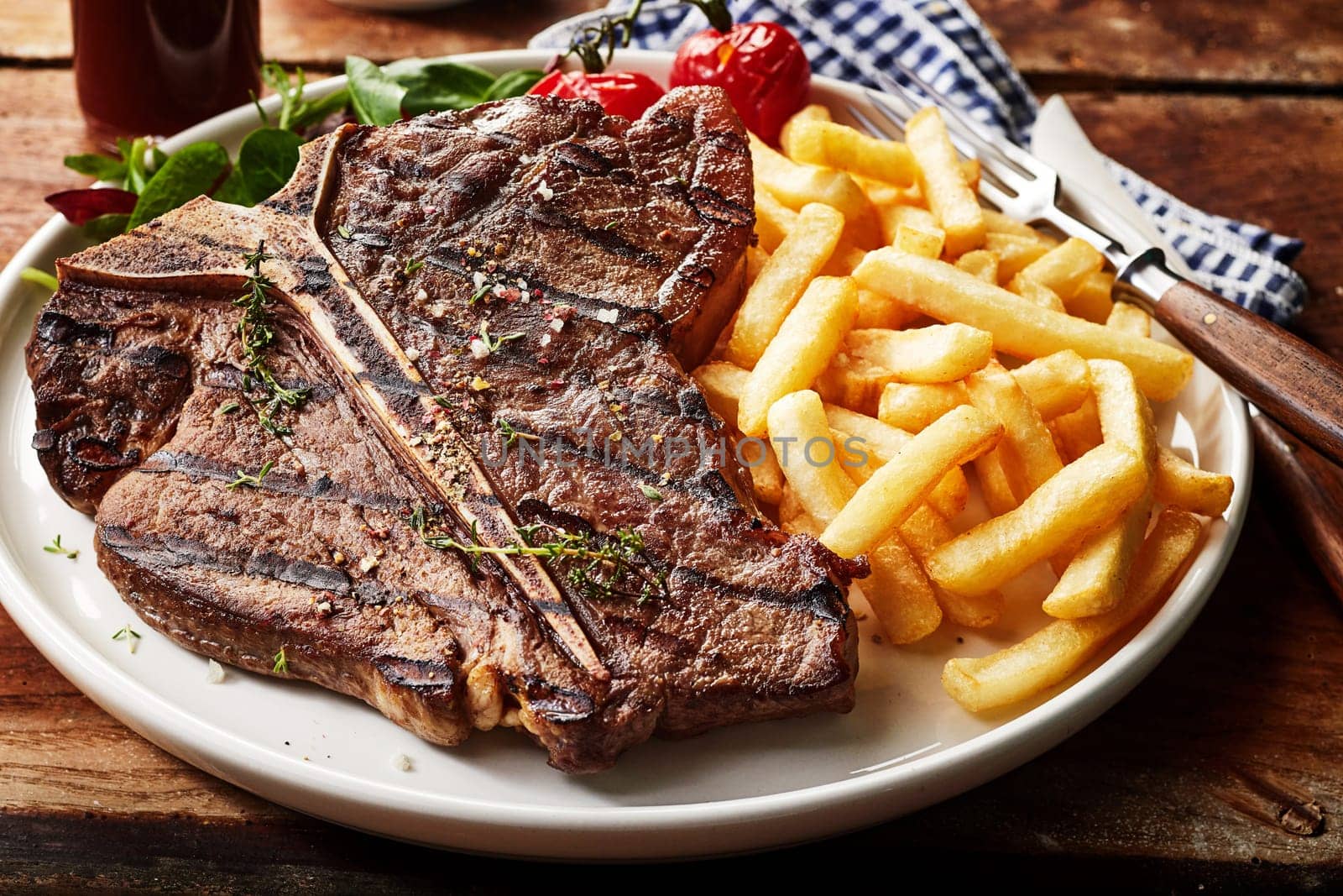 Tasty grilled T-bone steak seasoned with herbs and spices served with deep fried potato chips and salad in a close up view for menu advertising