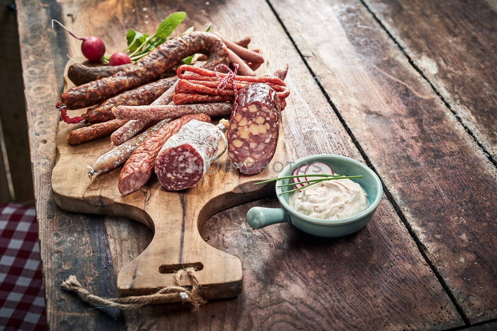 Buffet selection of dried spicy wild venison sausages on an old wooden board on a rustic table with a side dip or dressing and copy space