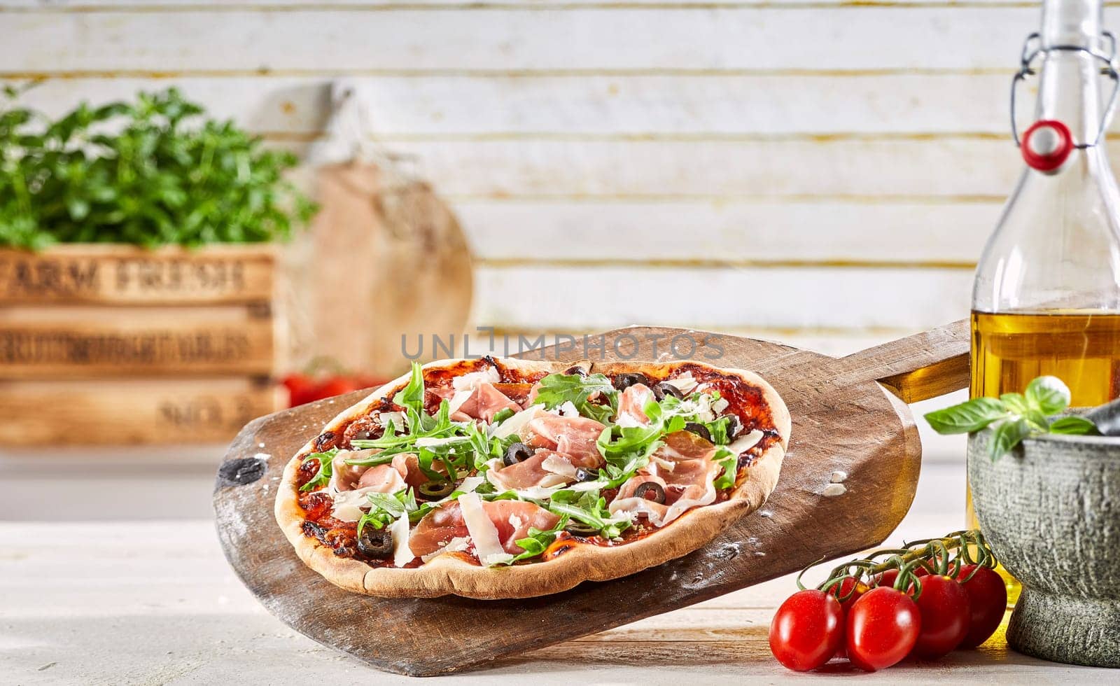Fresh oven-fired Prosciutto pizza served on an old wooden paddle at a pizzeria with ingredients and pestle and mortar alongside