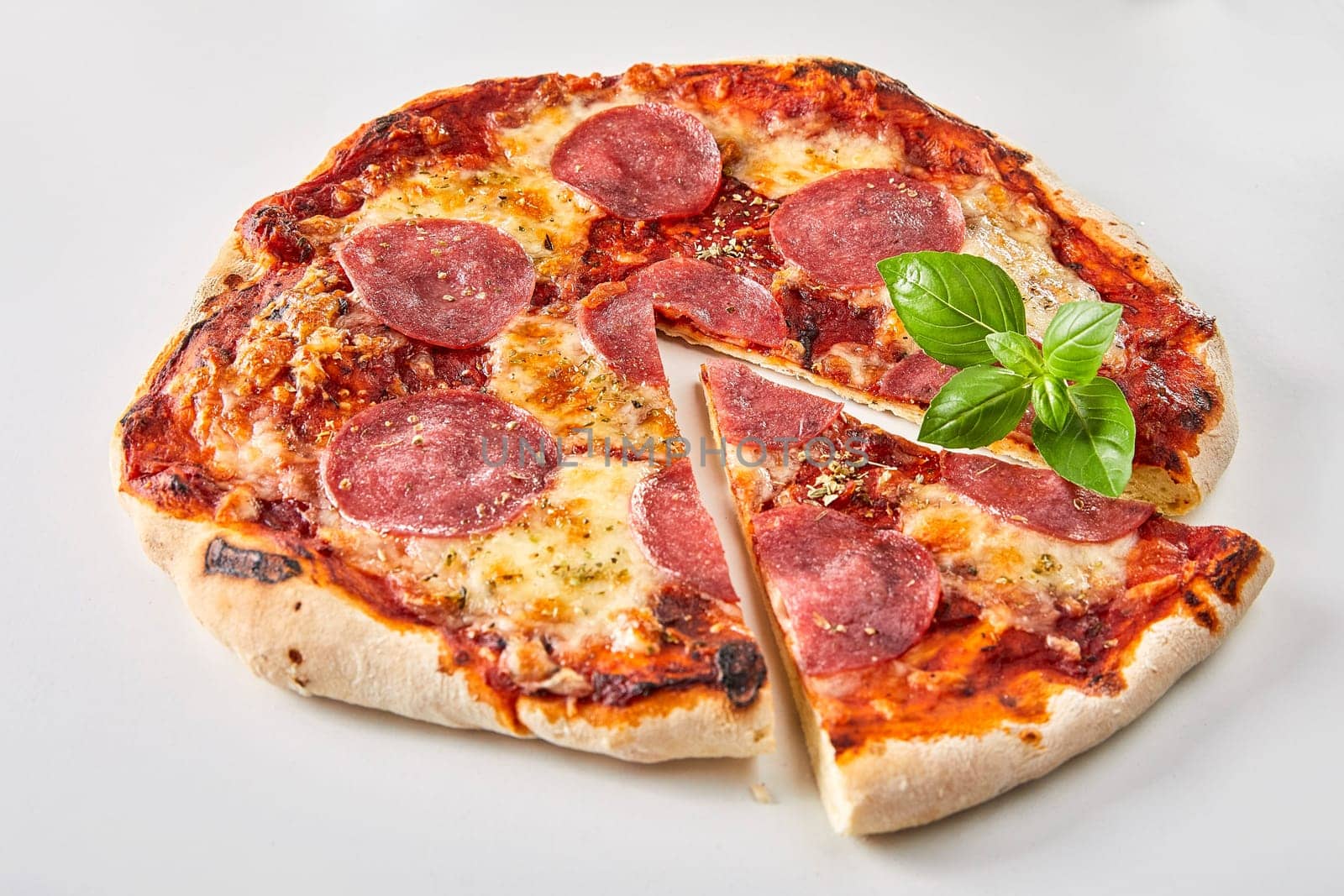 Sliced Italian salami pizza garnished with fresh basil over a white background for advertising or a menu