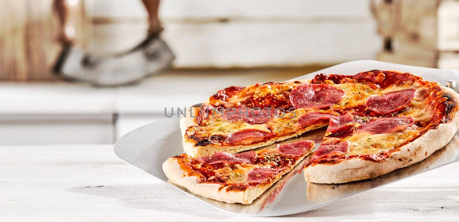 Freshly prepared Italian salami pizza served on a metal paddle in a pizzeria with a wedge portion cut out as a tasty snack or lunch