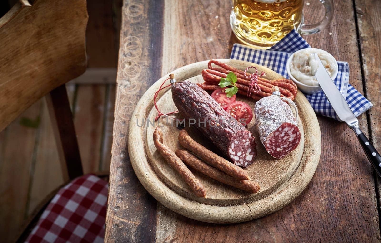 Assortment of wild venison spicy cured and dried sausages on a round wooden board on a rustic pub table with tankard of beer in a high angle view suitable for a menu