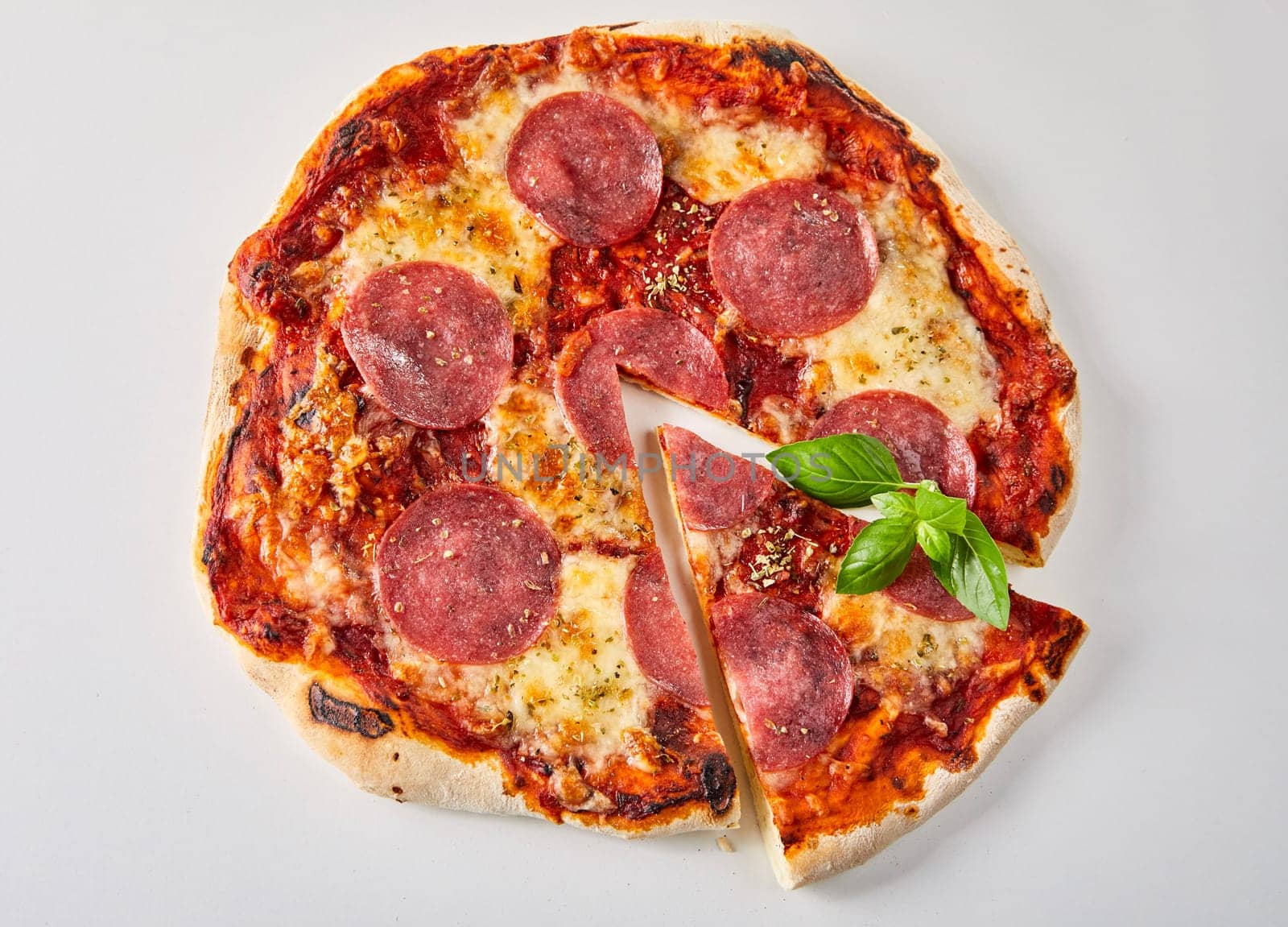 Sliced pepperoni pizza with fresh basil leaves, melted mozzarella and tomato paste seasoned with herbs viewed from above isolated on white