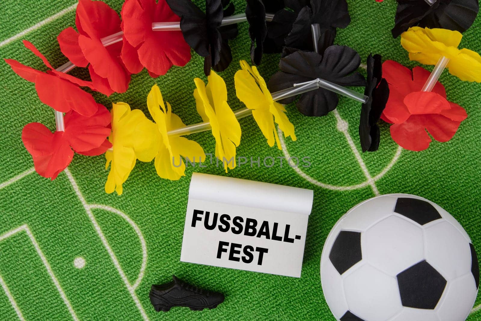 Fussballfest in german language means Soccer Festival. Soccer Ball with flower necklace in the colors of german flag and calendar