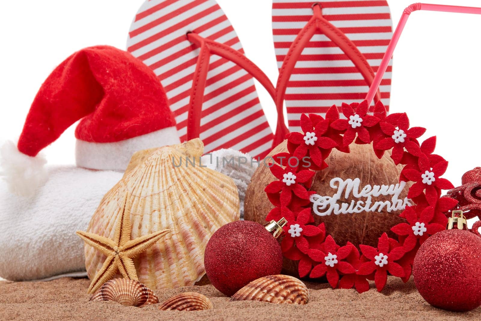 Still life with beach accessories (flip flops, towel, seashells, sand, coconut) and christmas ornaments on white background. Christmas. Winter vacation in warm countries, beach holiday