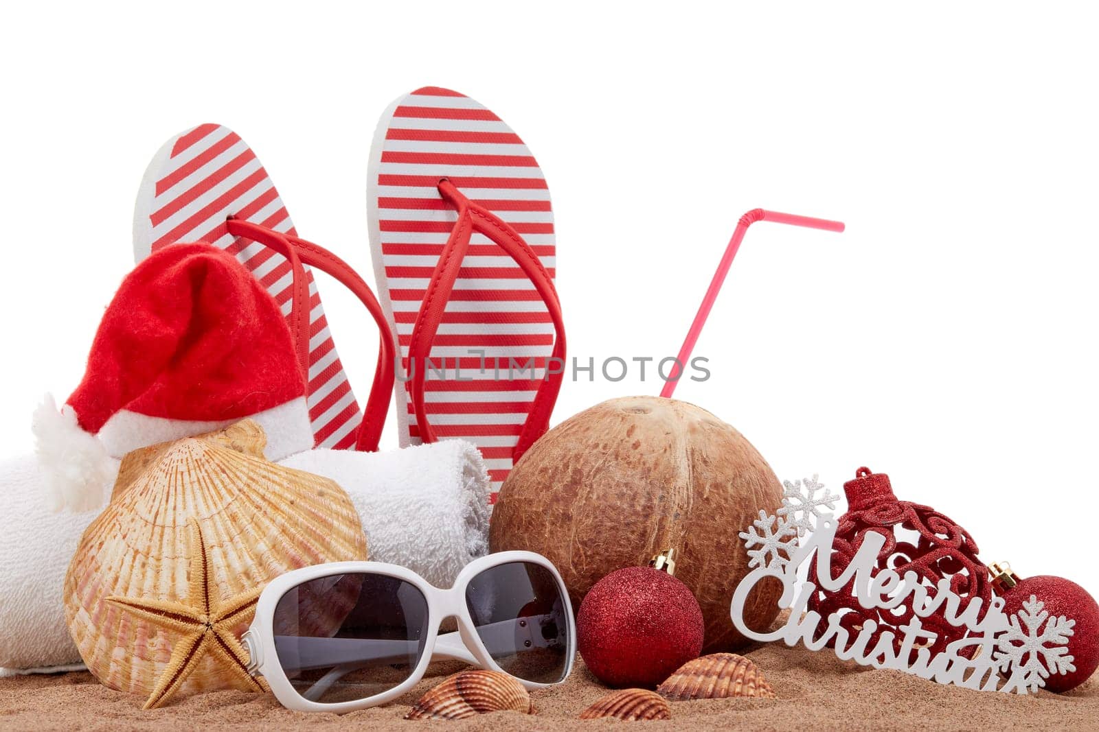 Still life with beach accessories (flip flops, towel, seashells, sand, coconut) and christmas ornaments on white background. Christmas. Winter vacation in warm countries, beach holiday