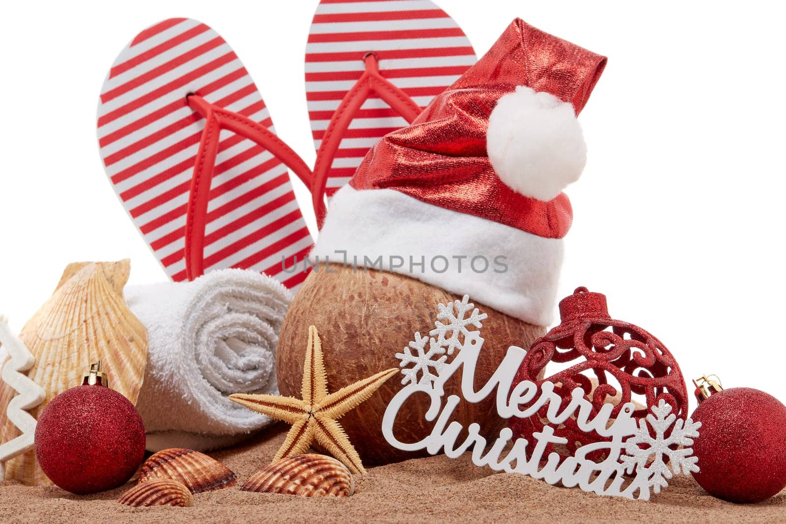 Still life with beach accessories (flip flops, towel, seashells, sand, coconut) and christmas ornaments on white background. Christmas. Winter vacation in warm countries, beach holiday