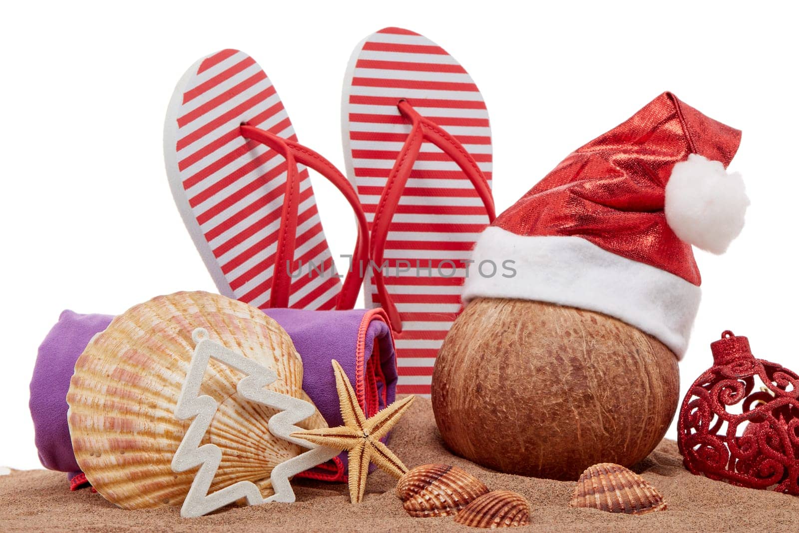 Still life with beach accessories (flip flops, towel, seashells, sand, coconut) and christmas ornaments on white background. New Year and Christmas. Winter vacation in warm countries, beach holiday
