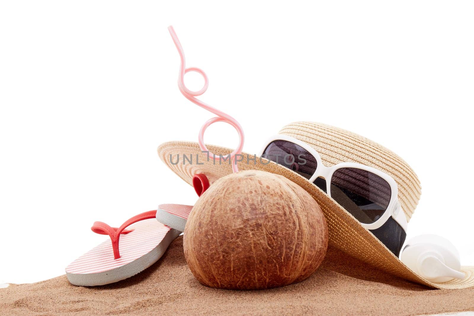 Beach accessories: flip flops, straw hat, sunglasses, sunscreen and coconut, lying on the sand on white background. Concept of sea vacation and travel. Summer background, Protection from uv