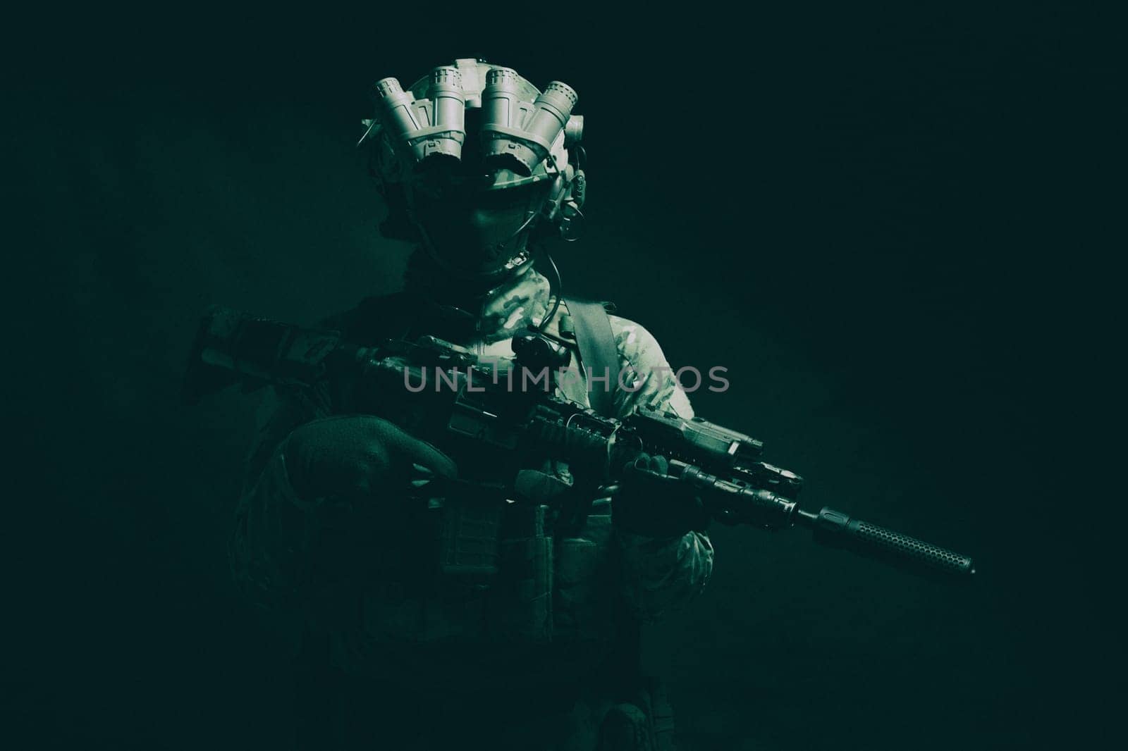 Half length, low key studio shoot of army soldier, marine infantryman in mask, camo uniform, equipped modern ammunition, armed service rifle standing in darkness with night vision device on helmet