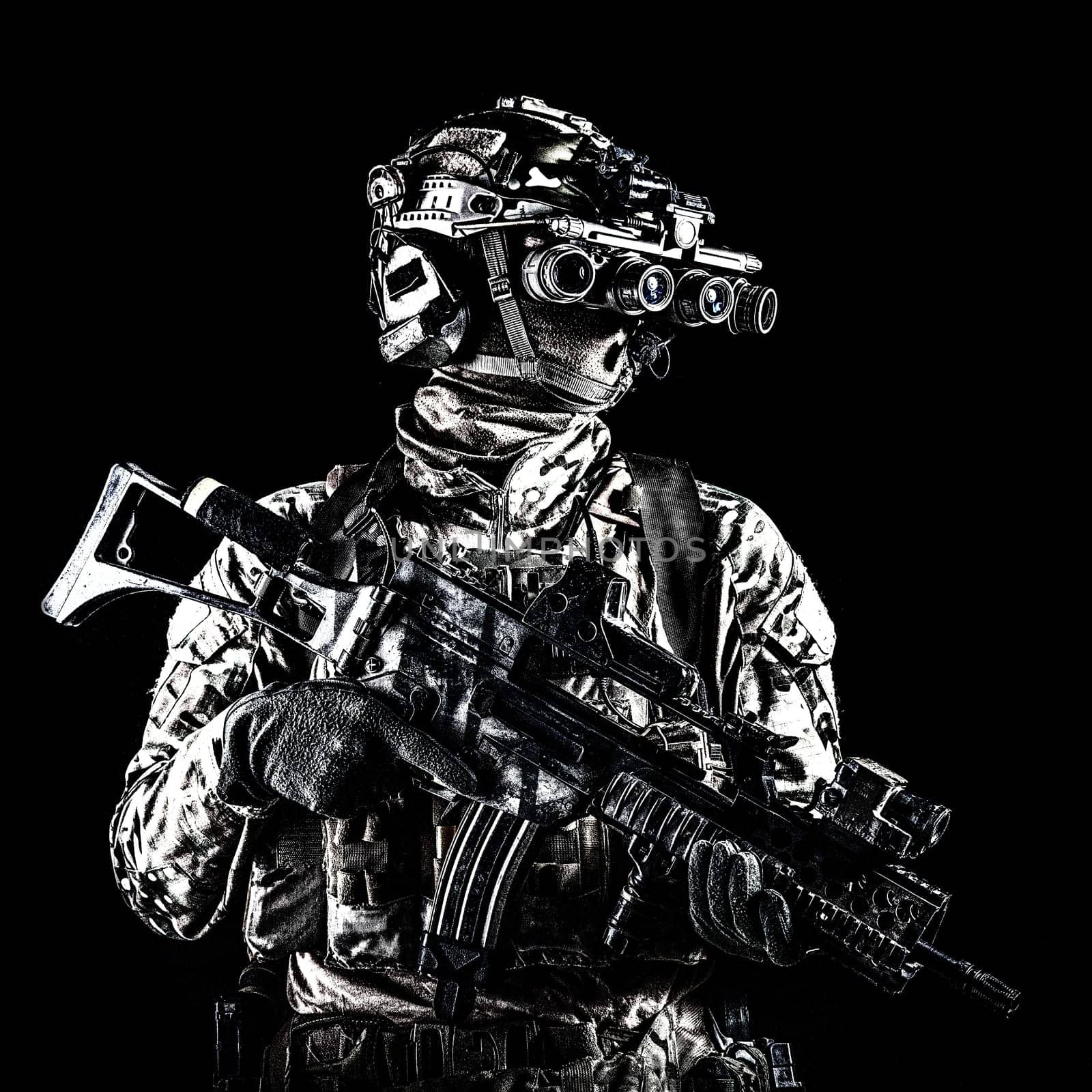 Marine rider in camouflage uniform and face mask, patrolling in darkness with quad-tube night vision goggles on battle helmet, holding modern assault rifle, low key studio portrait on black background