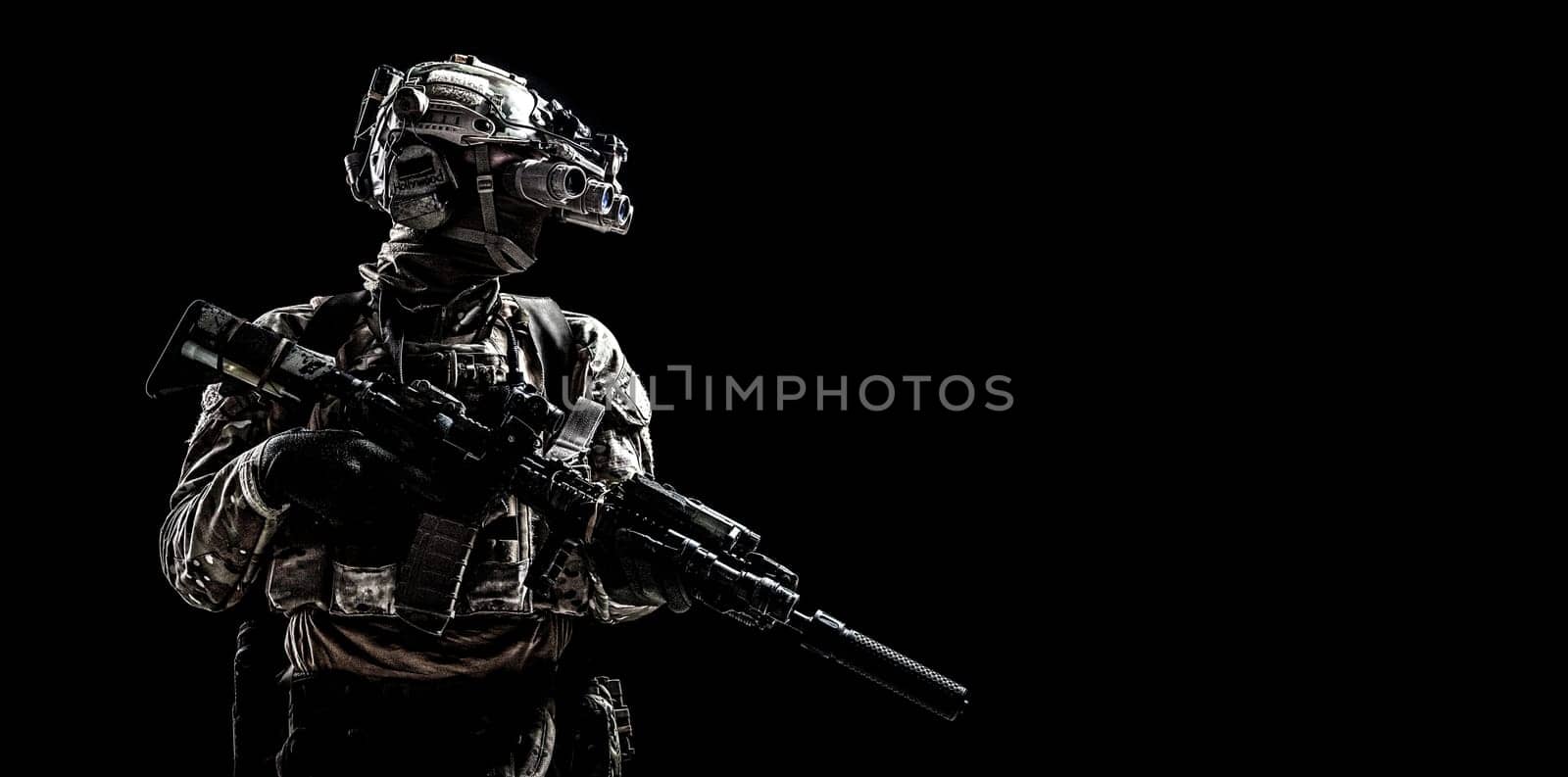 Modern army special forces equipped soldier, anti terrorist squad fighter, elite mercenary armed assault rifle, standing in darkness with night vision goggles on helmet, studio portrait, copyspace